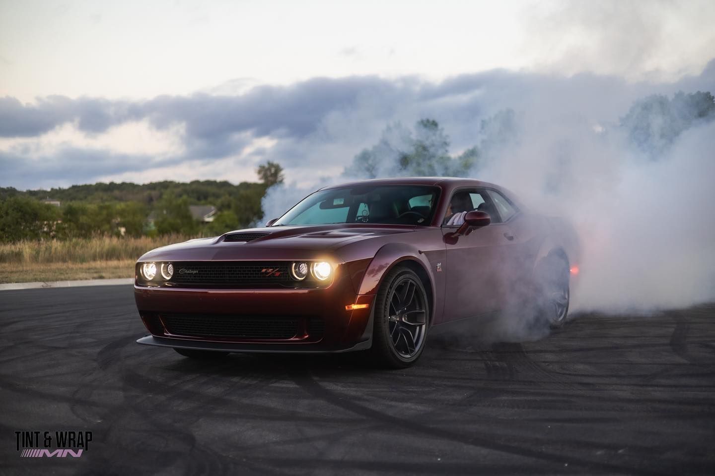 A red Dodge Challenger is doing a burnout on a track.