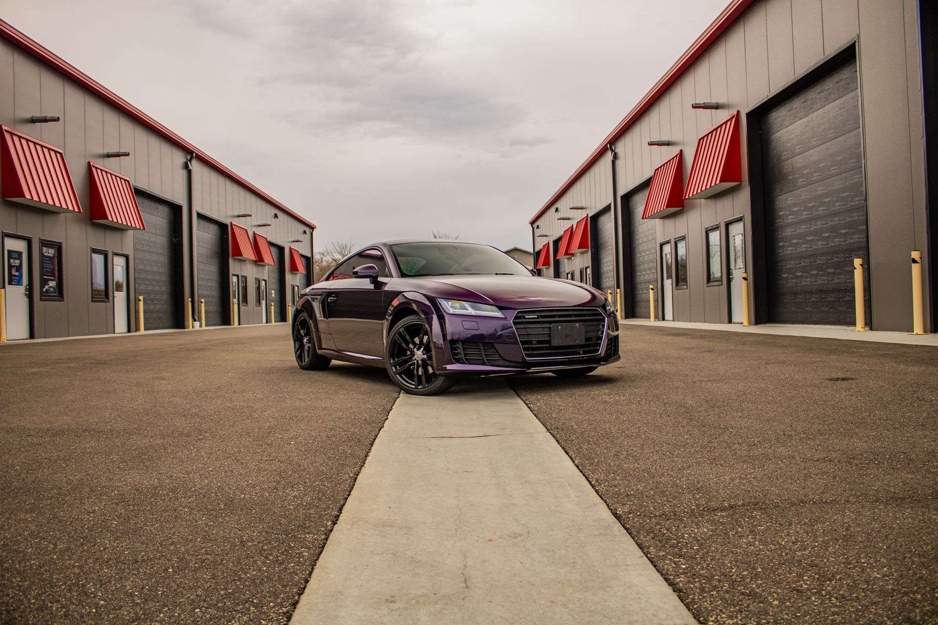 A purple car is parked in a parking lot between two buildings.
