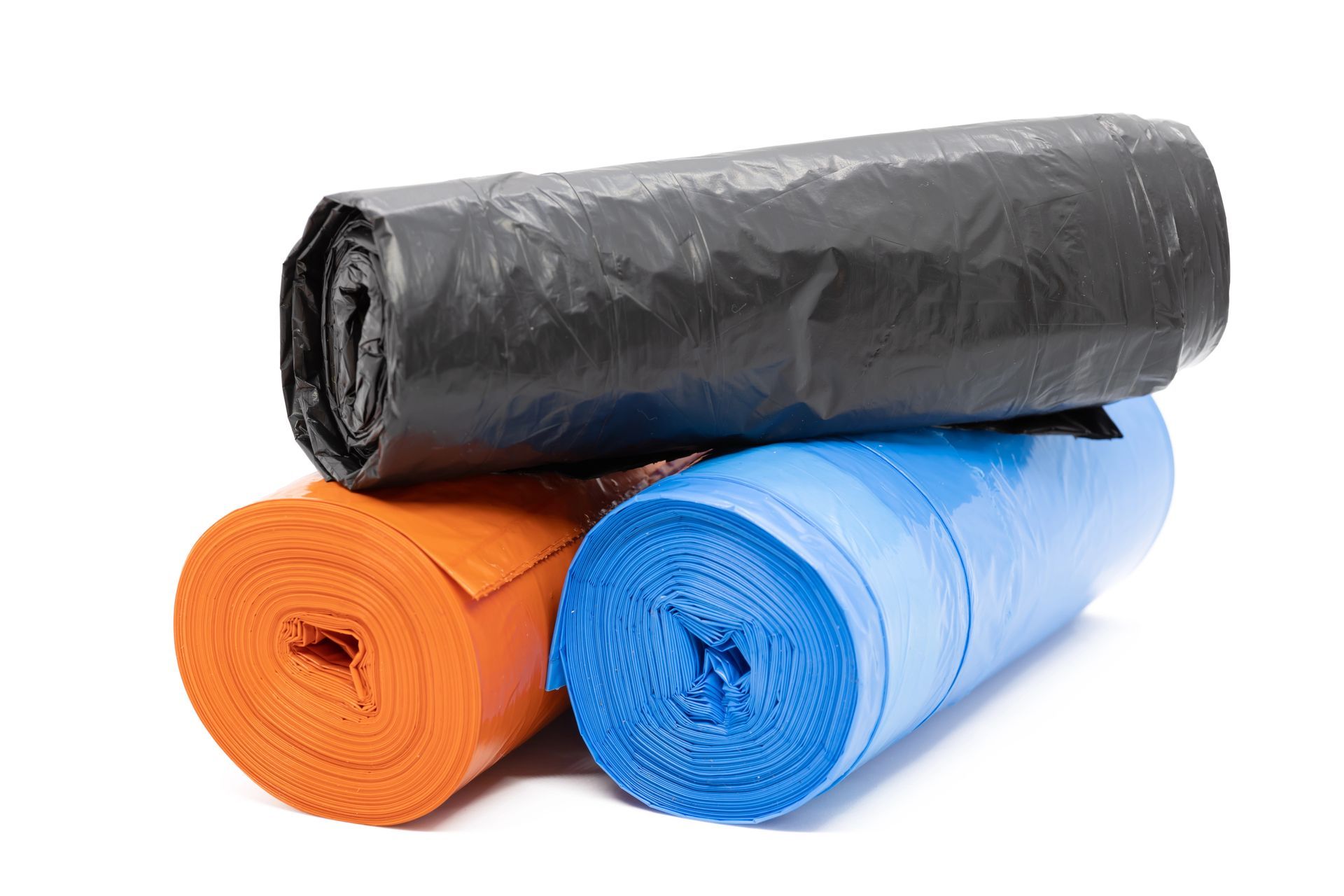 Tres rollos de bolsas de basura de colores: negro, azul y naranja, apilados sobre un fondo blanco.