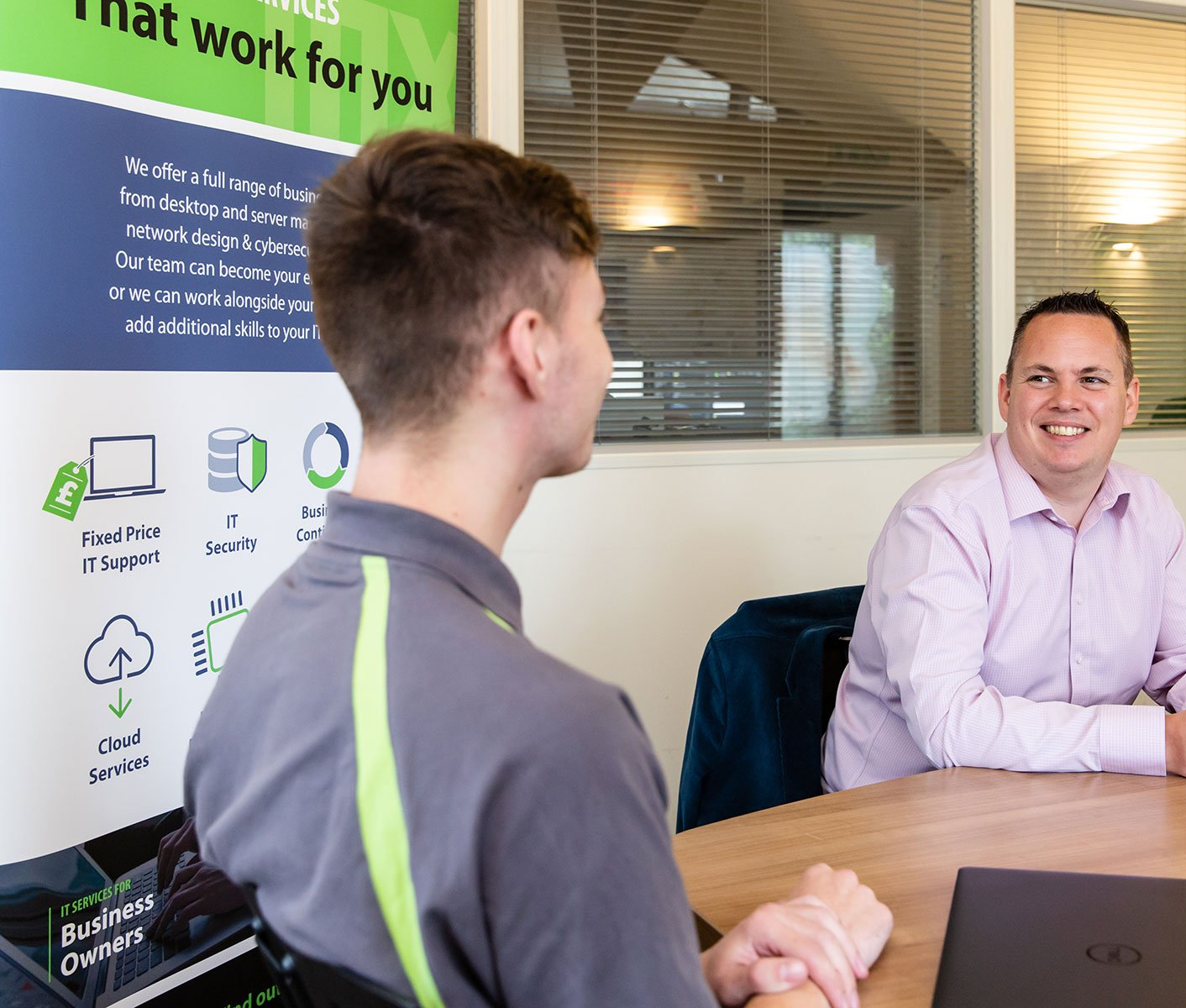 Two men are sitting at a table in front of a sign that says that work for you.