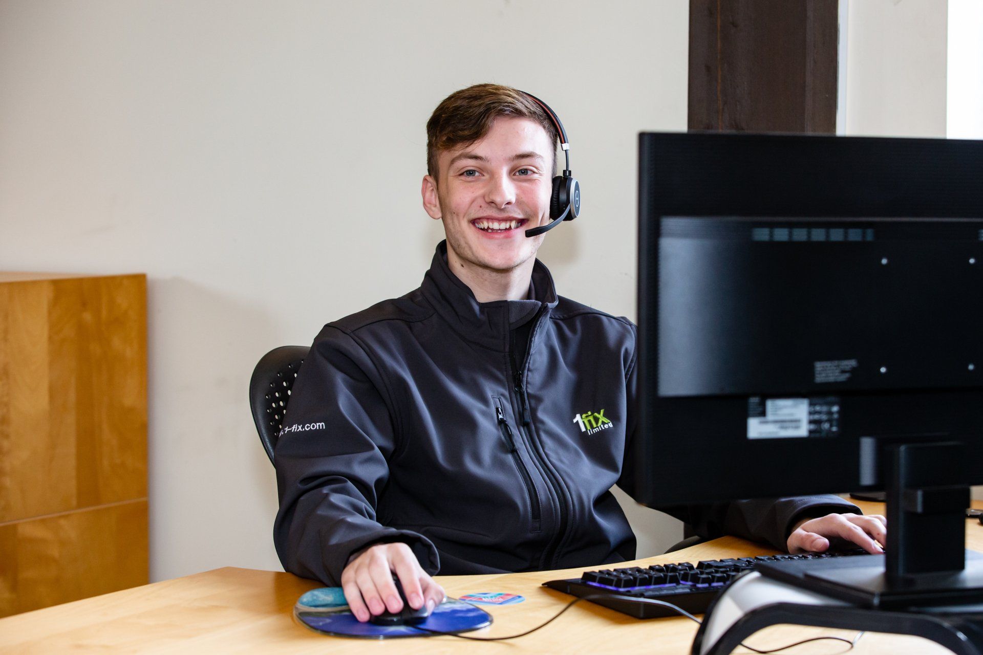 A young man wearing a headset is sitting at a desk in front of a computer.