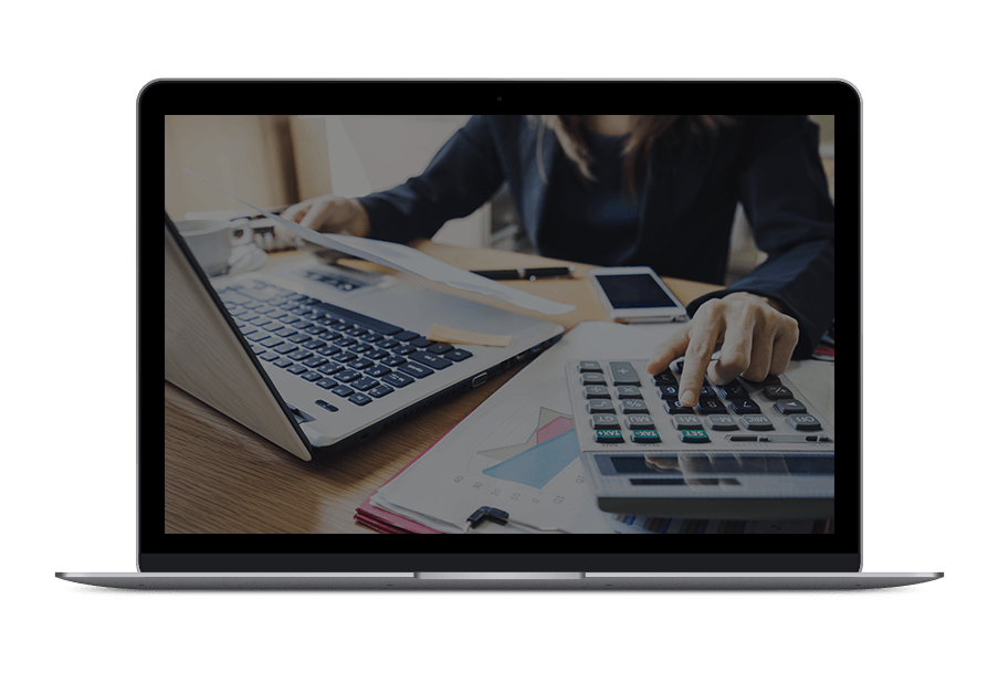 A woman is sitting at a desk using a laptop and a calculator.