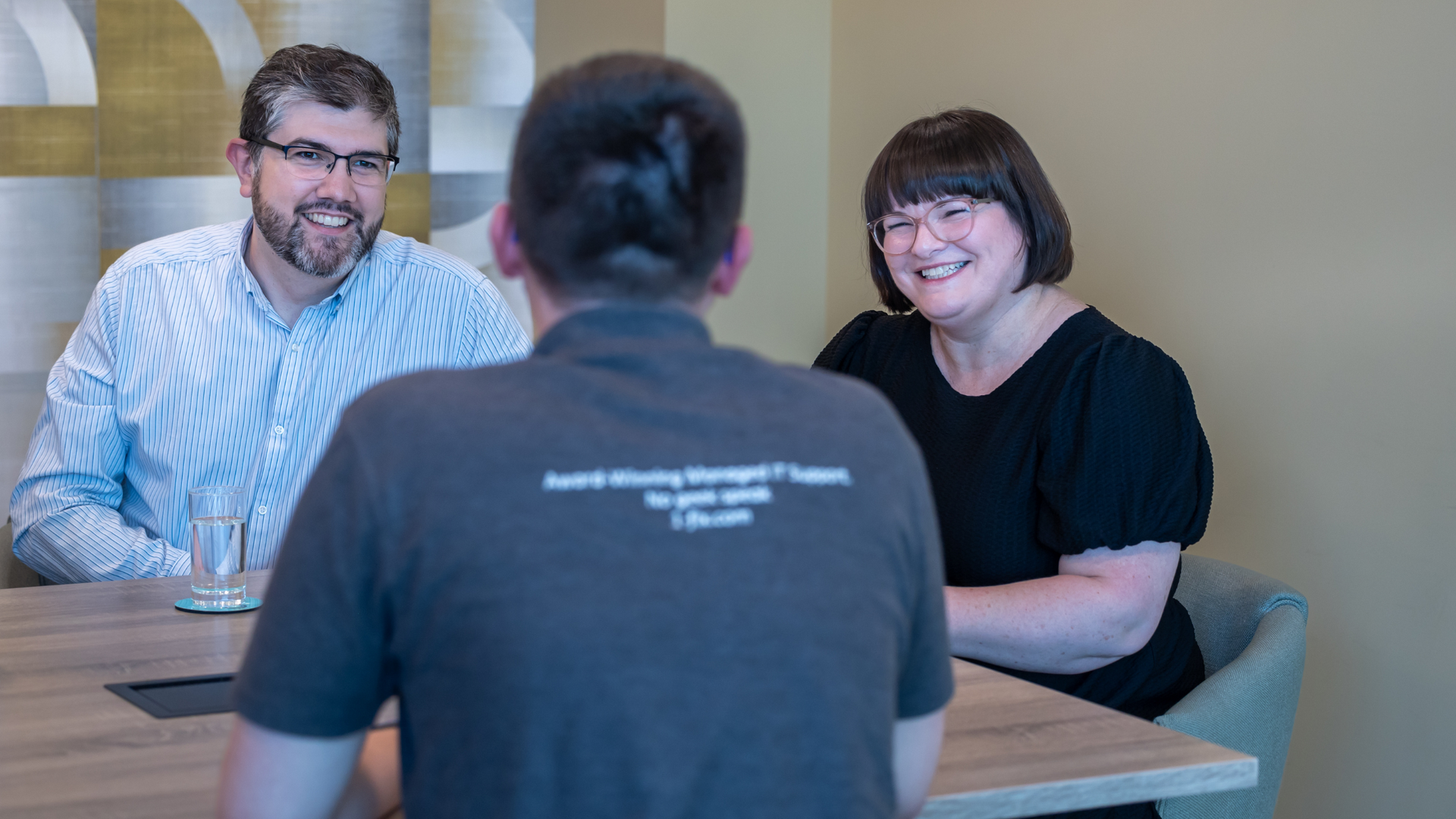 Photo of a male and a female smiling and looking at another male who is turned away from the camera.