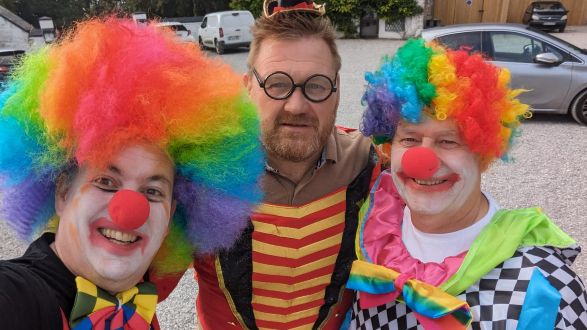 Three men dressed as clowns are posing for a picture in a parking lot.