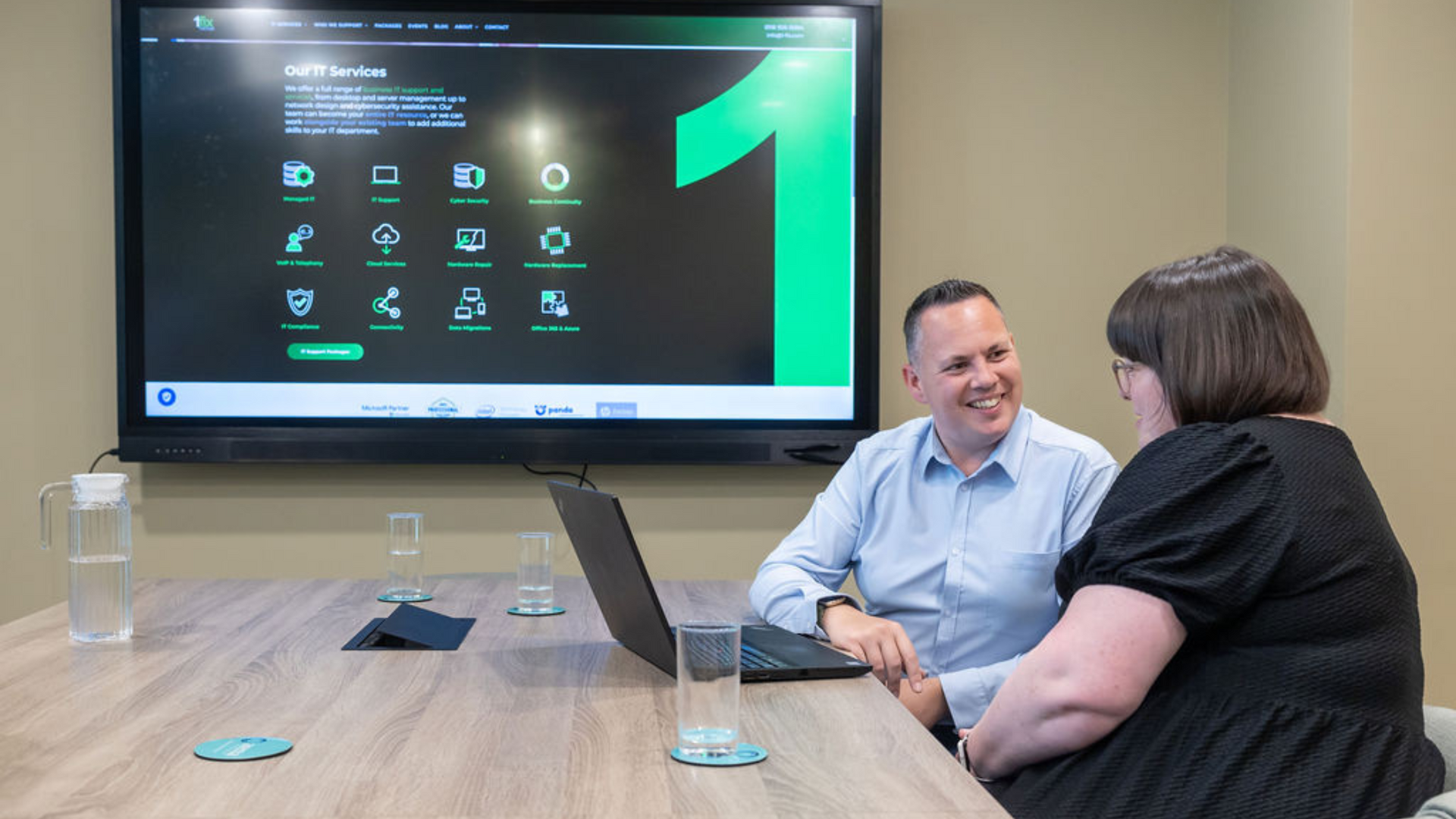 Photo of Jo and Craig talking on a desk with a laptop open. 