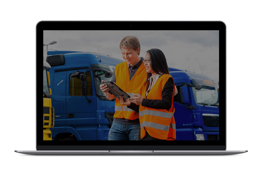 A man and a woman are looking at a tablet in front of trucks.