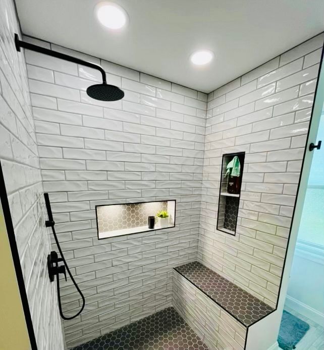 Modern tiled shower with built-in bench, two niches, and black fixtures. White textured tiles, gray floor.
