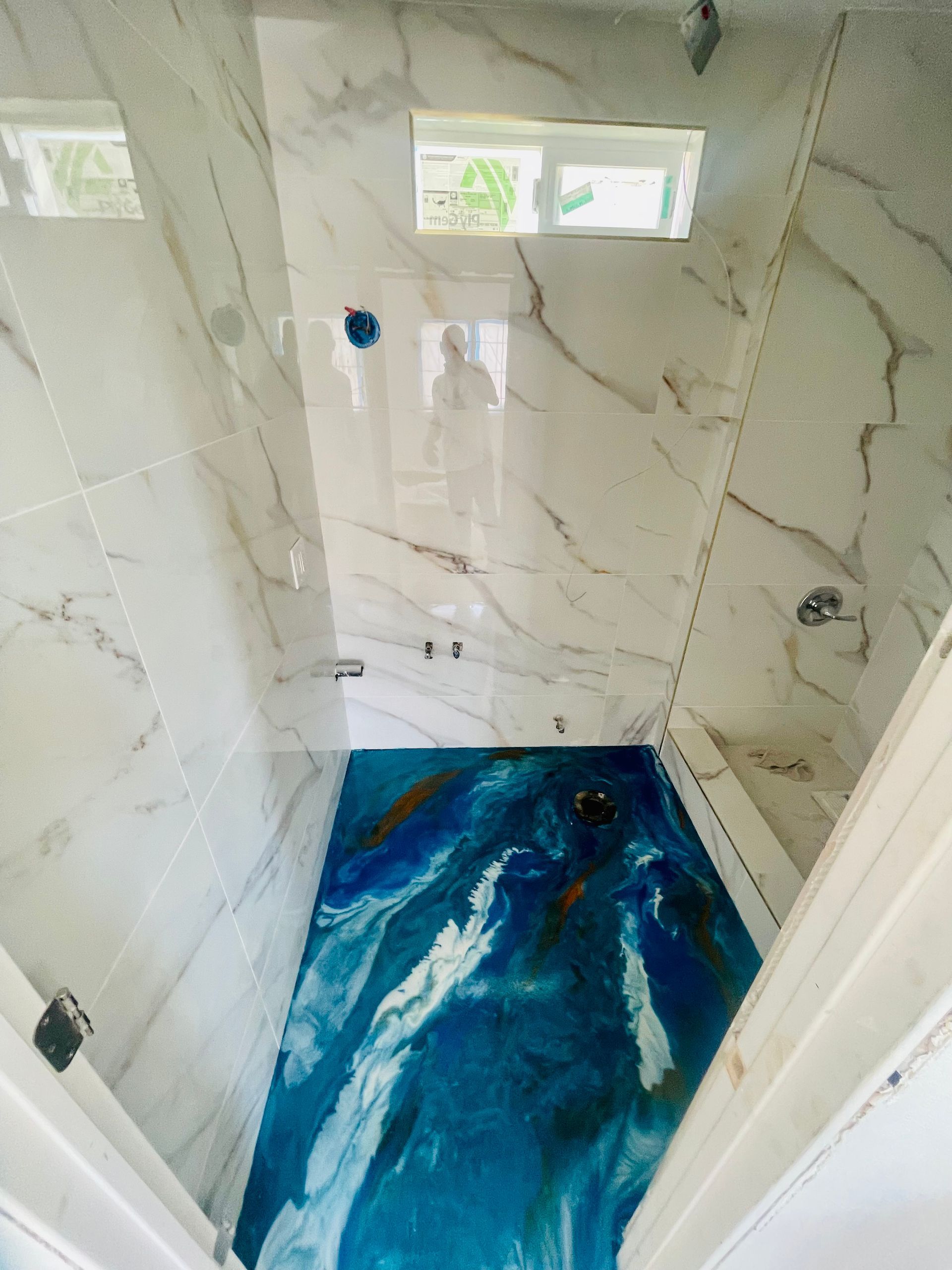 Bathroom with blue and white epoxy floor, white marble walls, and small window.