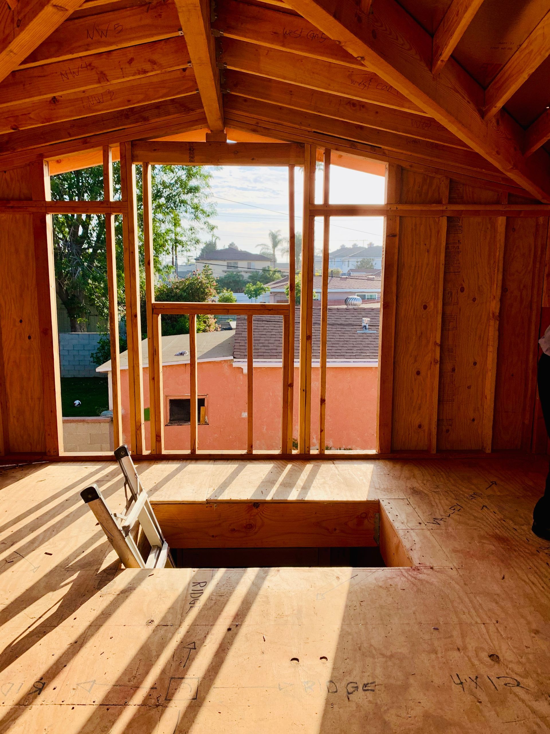 Interior view of unfinished wooden attic space with window frame, and a hole in the floor.