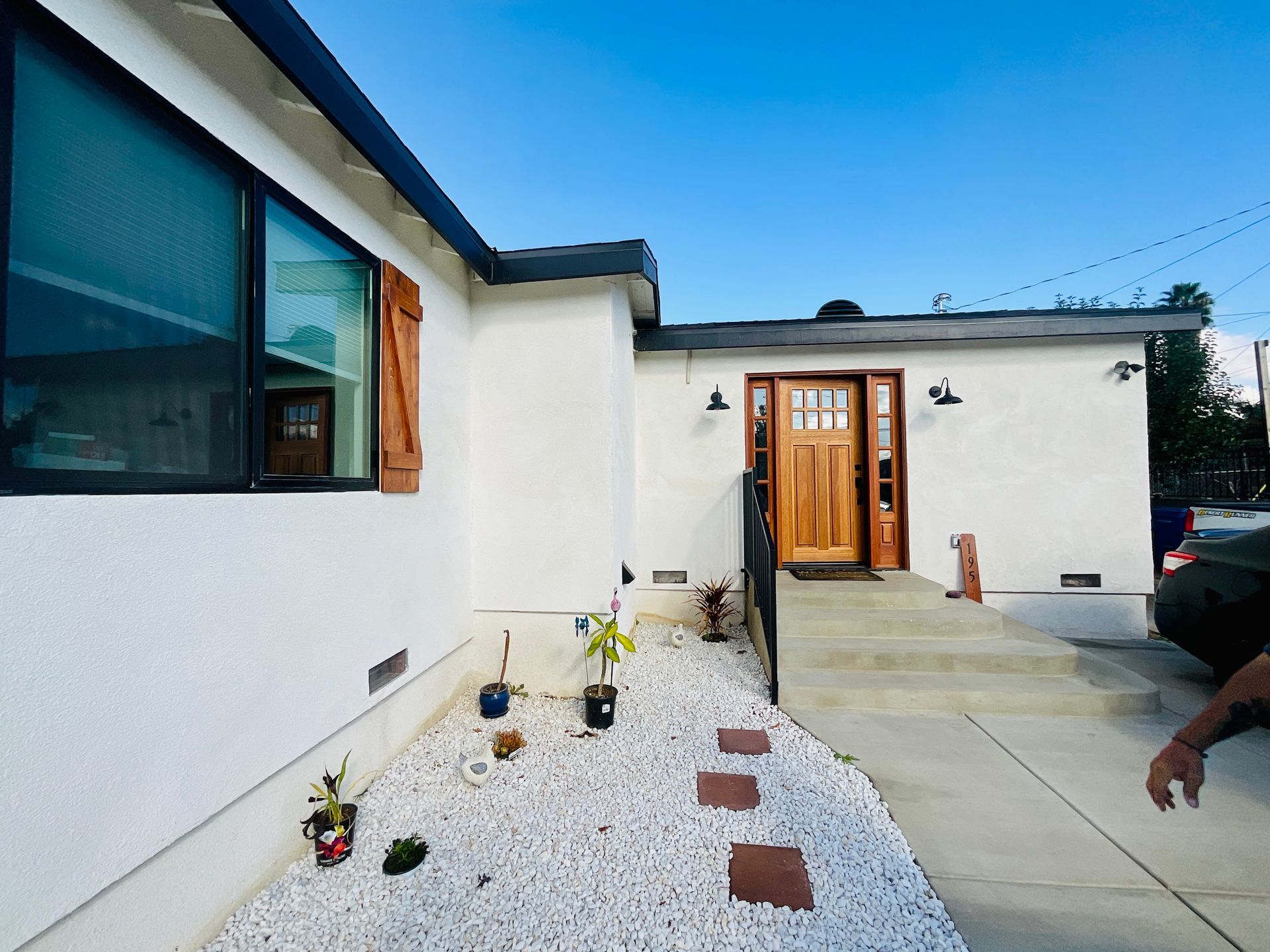 White house with wooden door and shutters, pathway, small garden, blue sky.