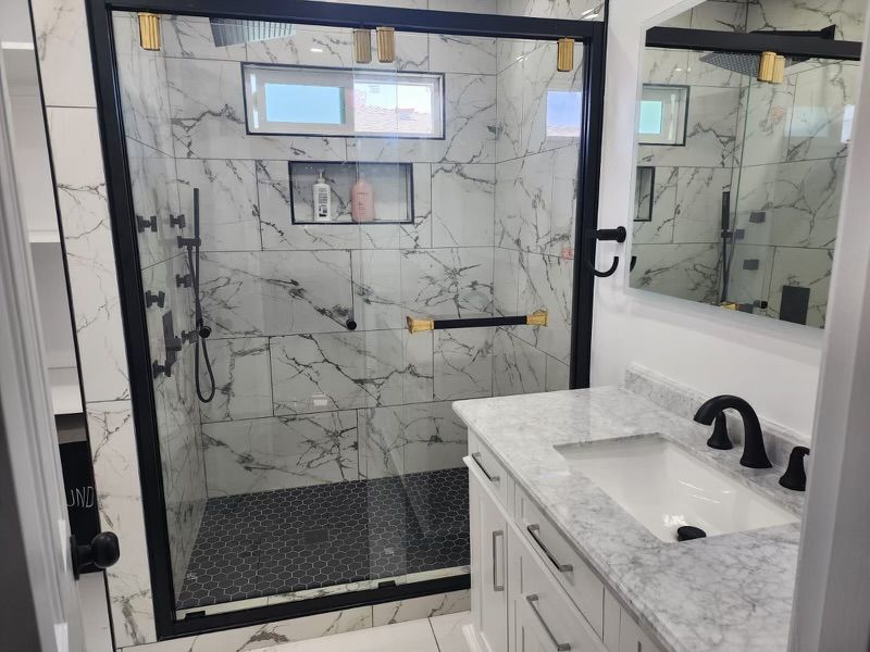 Bathroom with marble tile shower, black trim, and white vanity with a black faucet.