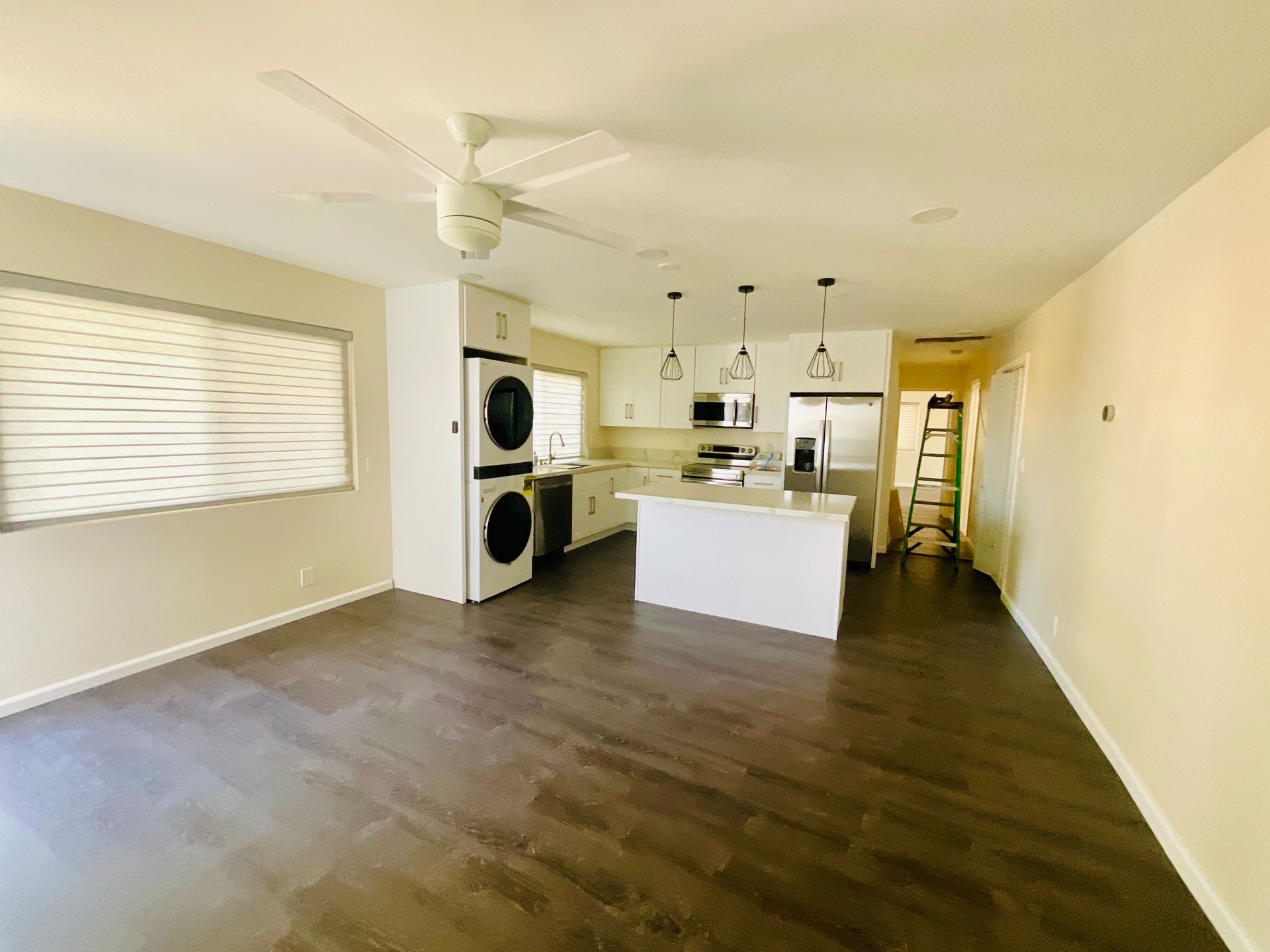 Open-plan kitchen and living area with white cabinets, island, appliances, and dark wood-look flooring.