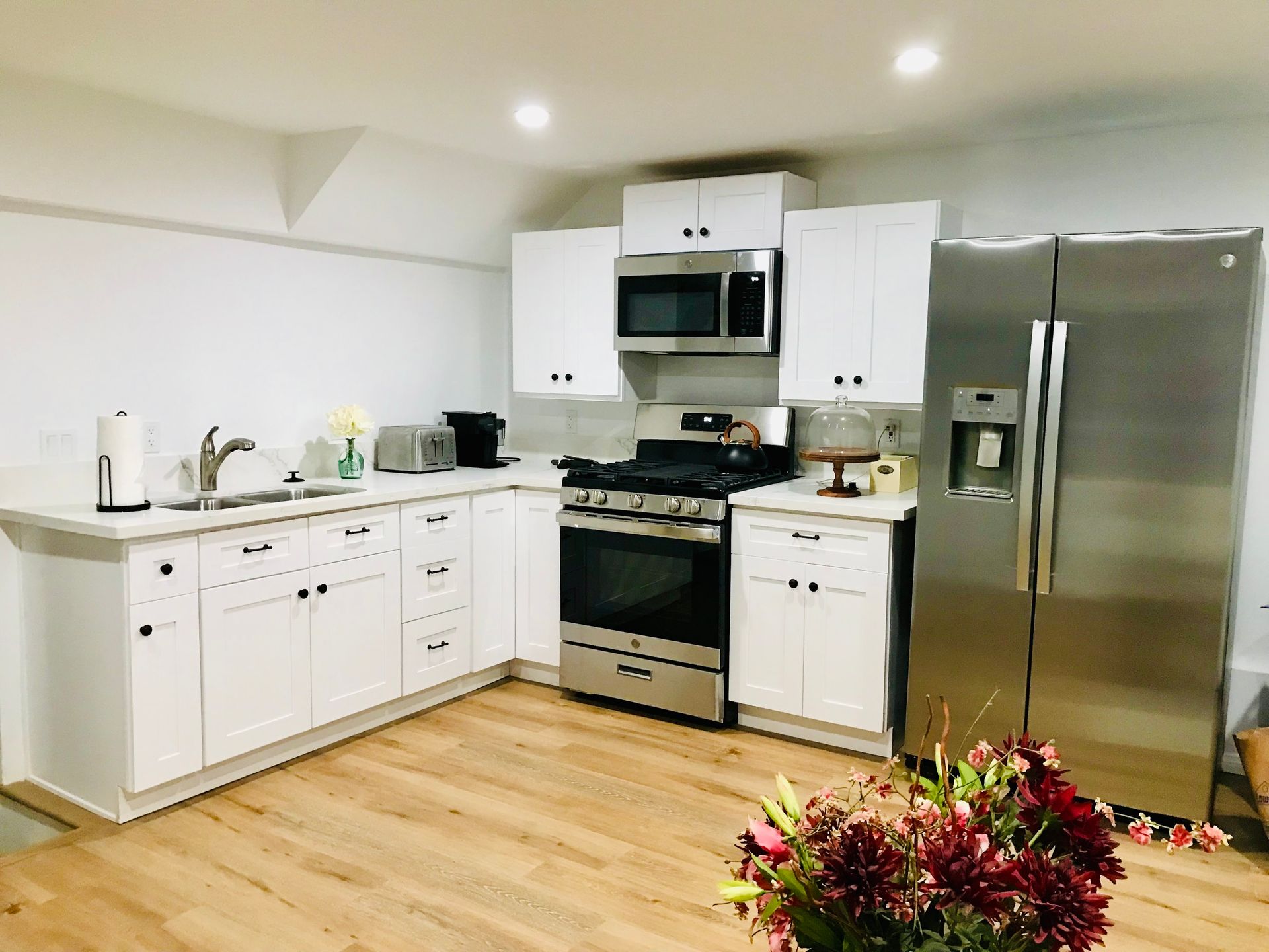 A modern white kitchen with stainless steel appliances and light wood floors.