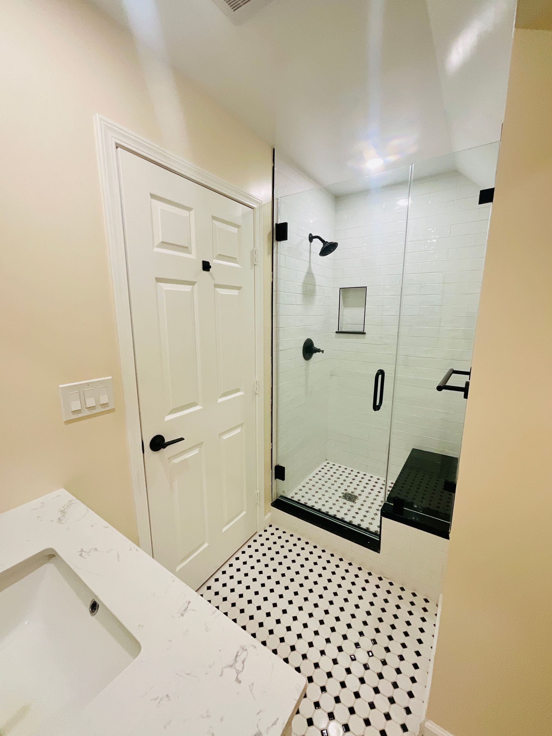 Bathroom with white and black tile, glass shower, black fixtures, and white vanity.