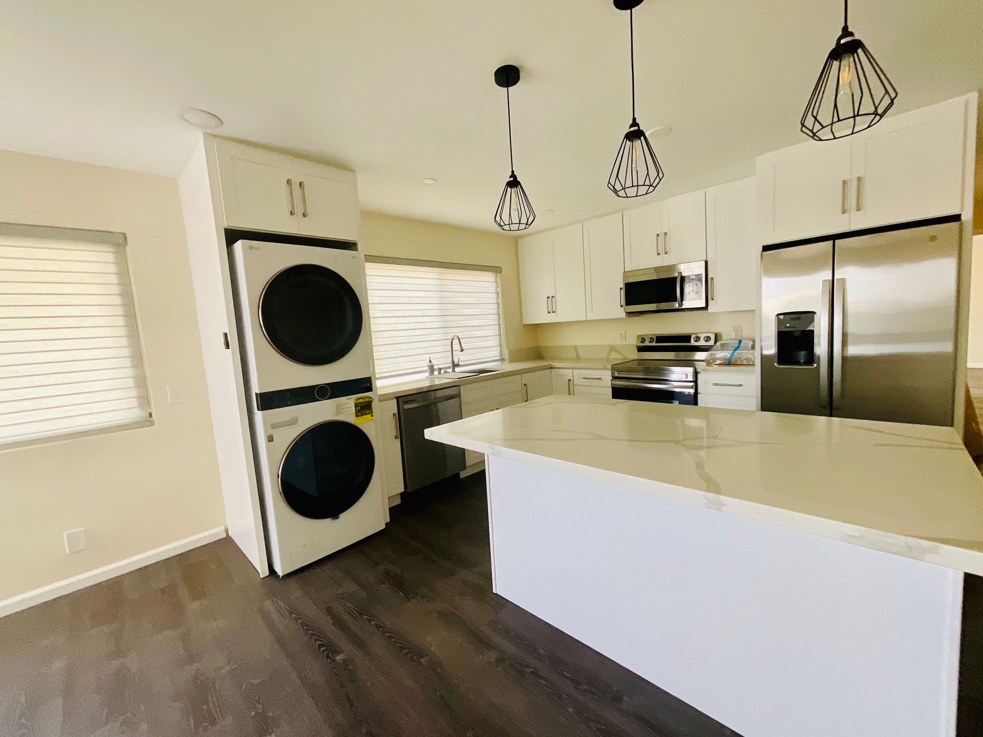 Modern kitchen with white cabinets, island, and stacked washer/dryer. Stainless steel appliances, pendant lights.