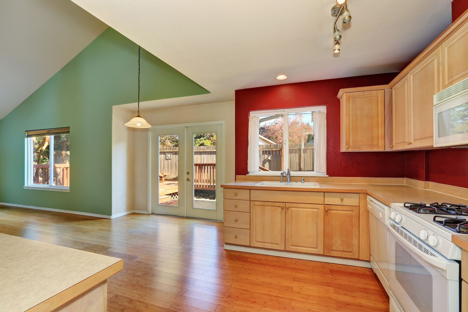 Kitchen with green and red walls, light wood cabinets, and French doors leading to a backyard.