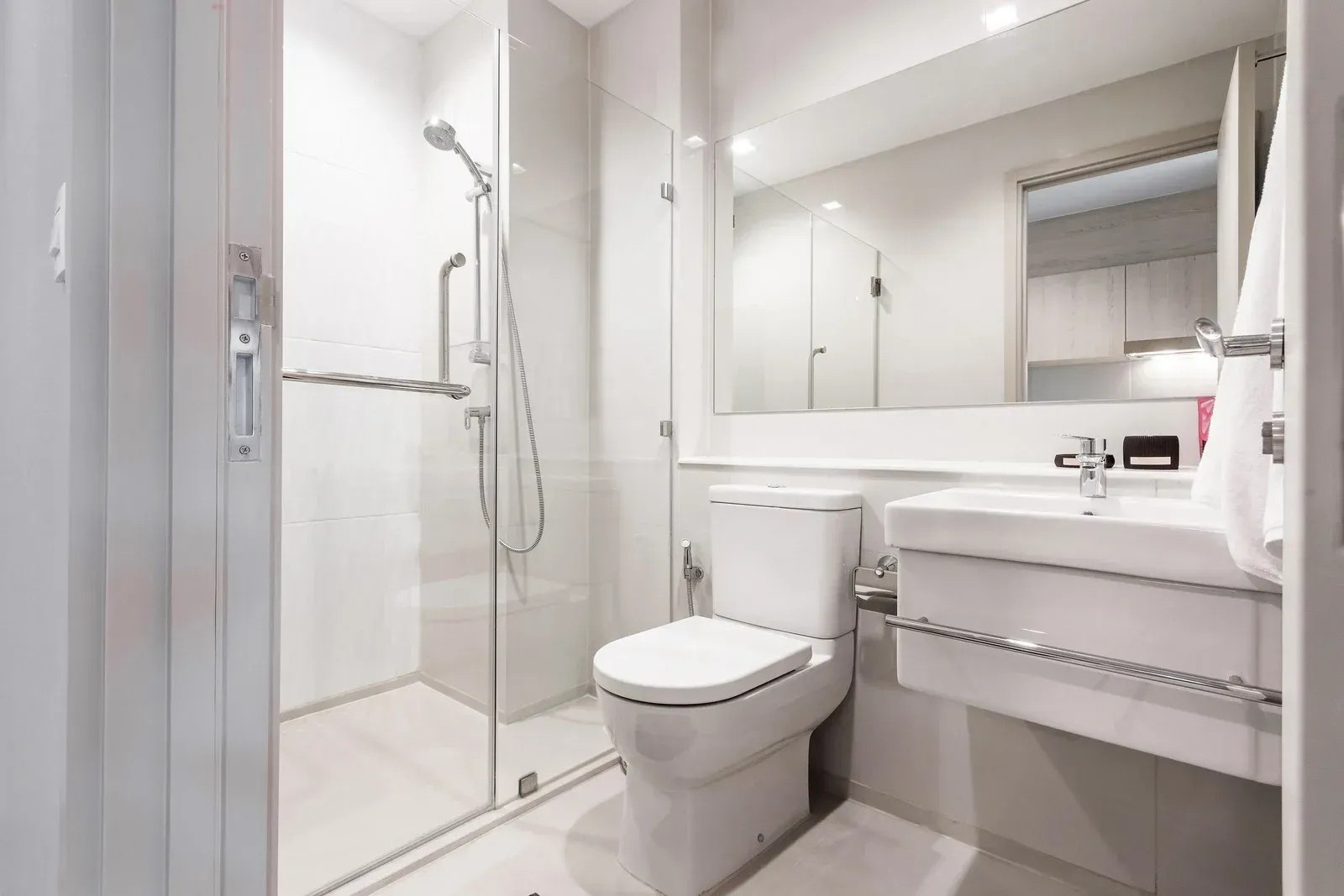 Modern, bright white bathroom with glass shower, toilet, and sink.