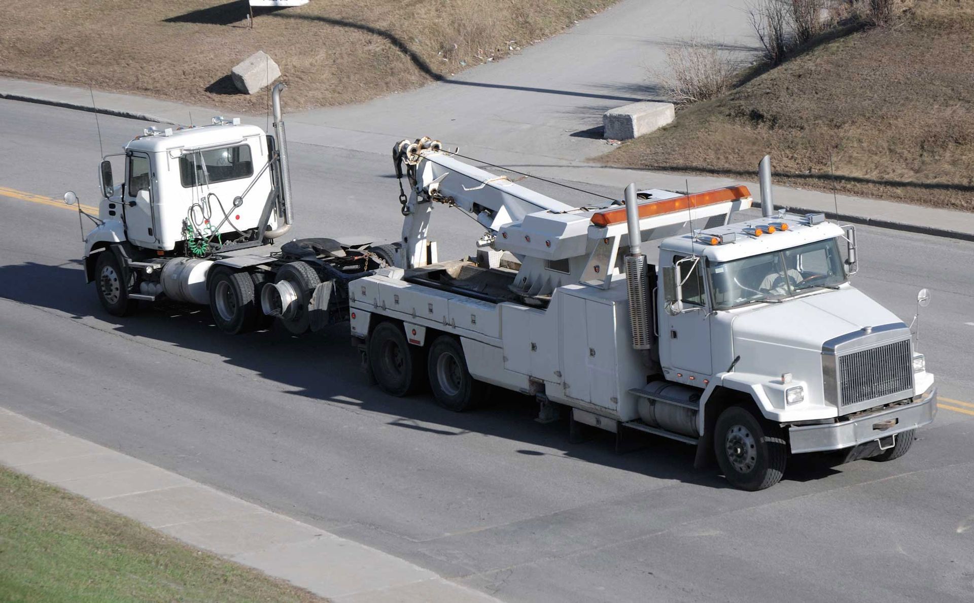 White heavy duty tow truck hauling a semi-truck on the roadside.