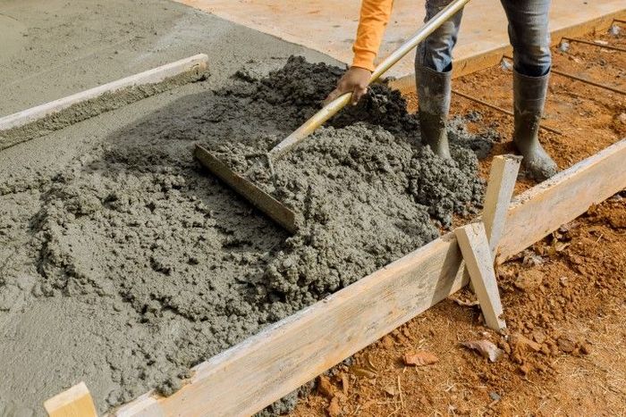 Person smoothing wet concrete with a rake at a construction site.