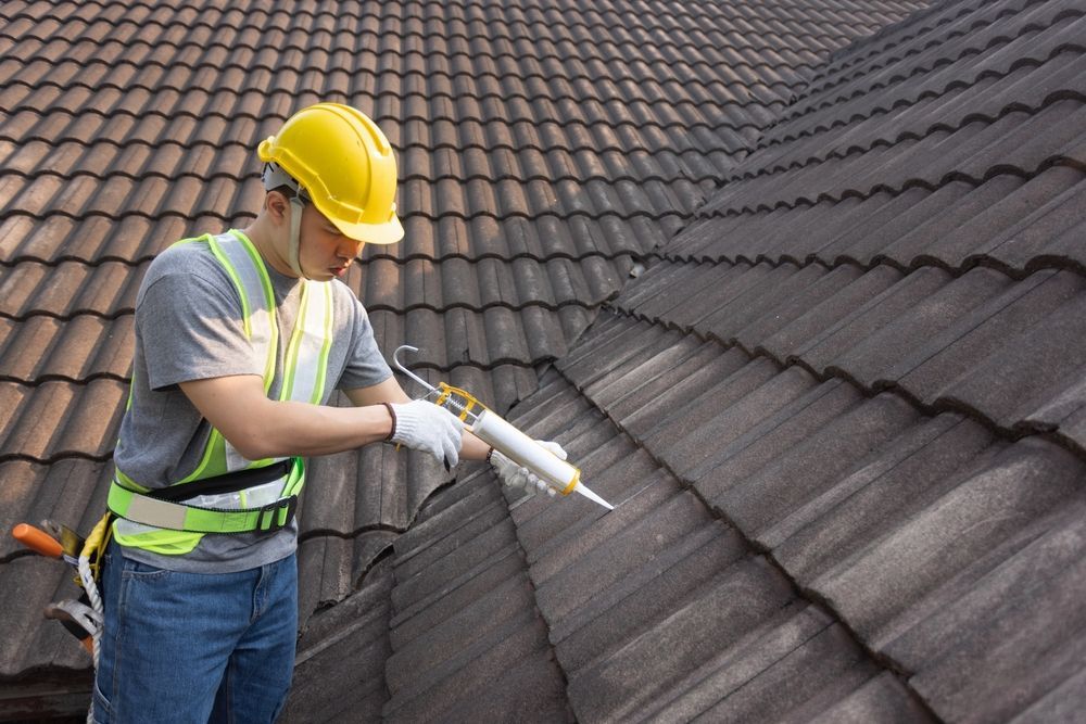 A man is applying sealant to a tiled roof.