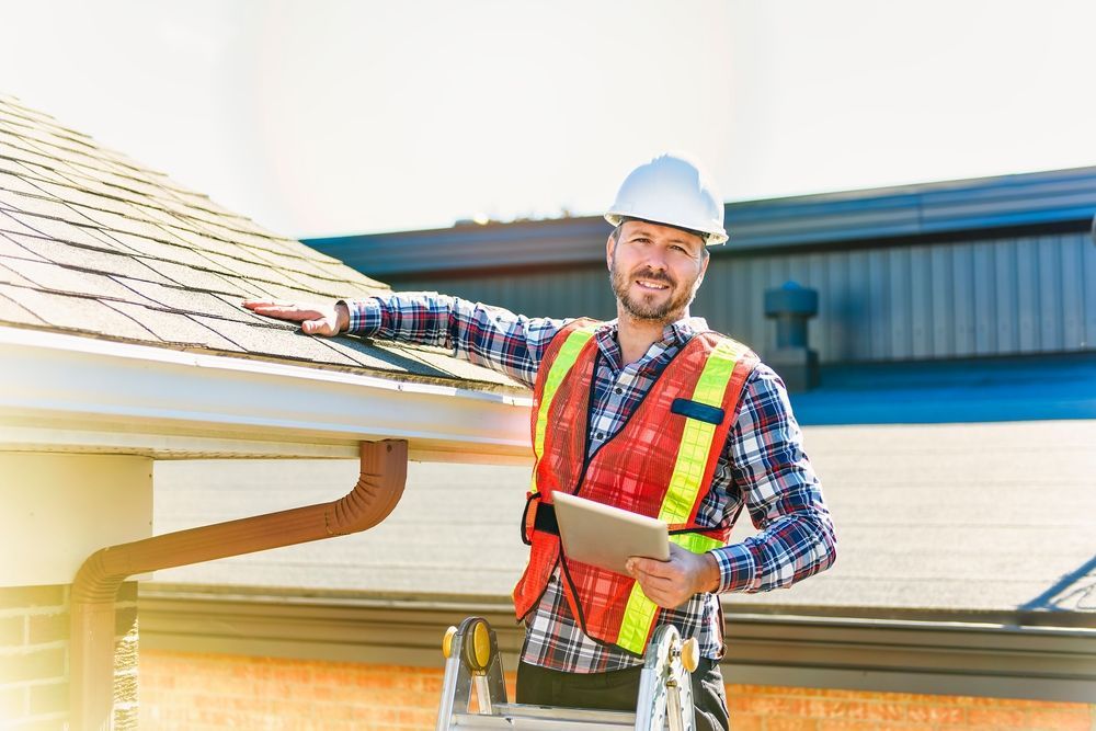 A man is standing on a ladder holding a tablet and pointing at a roof.