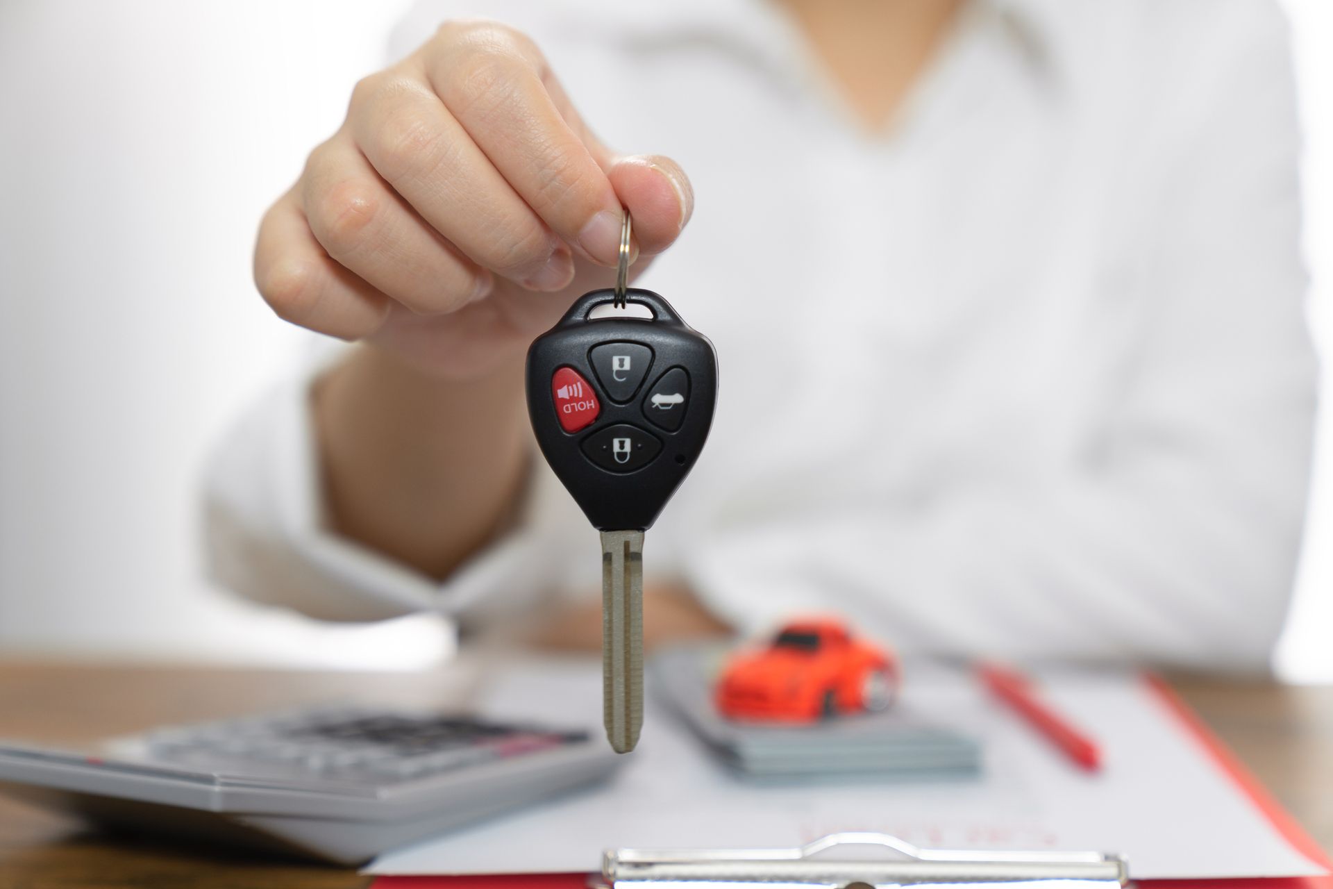 A woman is holding a car key in front of a calculator and clipboard.