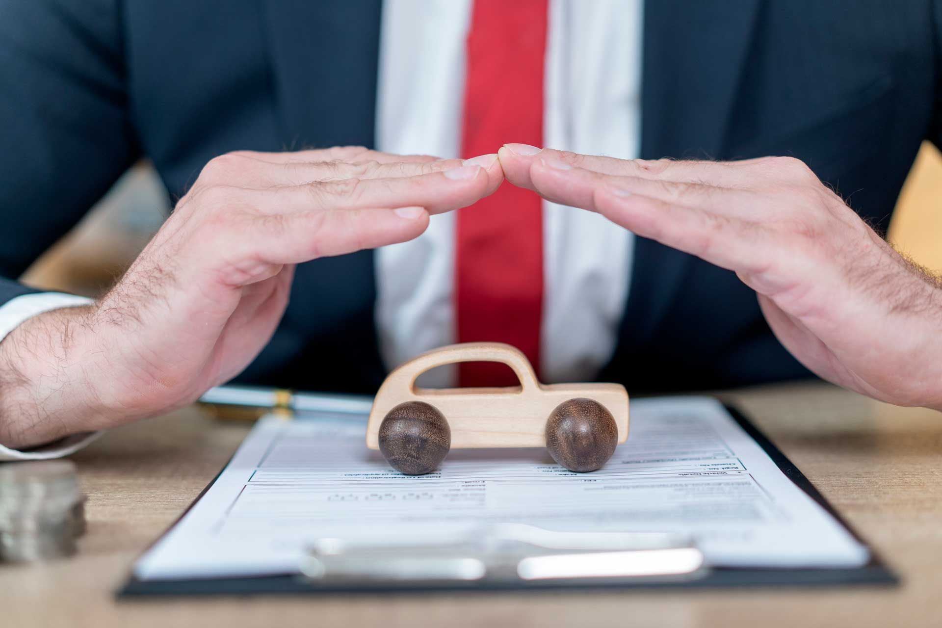 Vehicle insurance agent protecting car model with hands over policy documents.