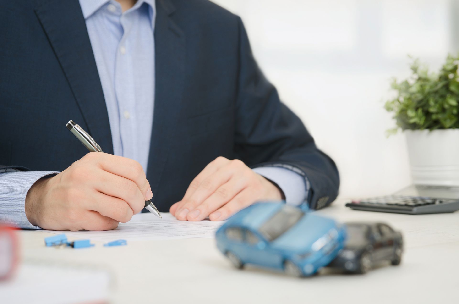 Insurance agent with a blue suit signs on a paper with a pair of blurry toy cars on front.