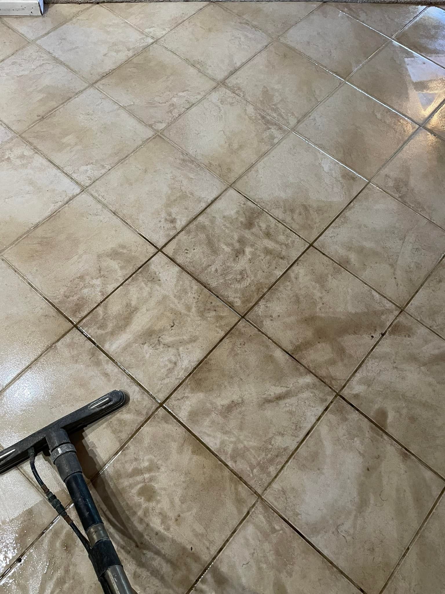 Wet tile floor being cleaned with a cleaning tool, showing dirty tiles with dark grout.