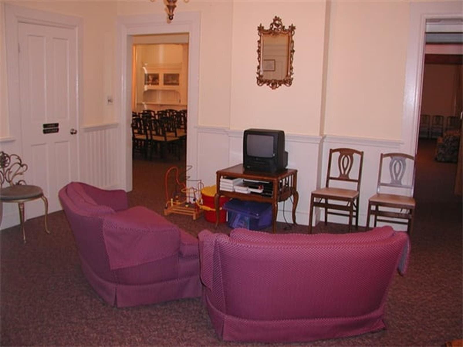 Two pink armchairs face a small television in a room with ornate chairs and another room visible in the background.