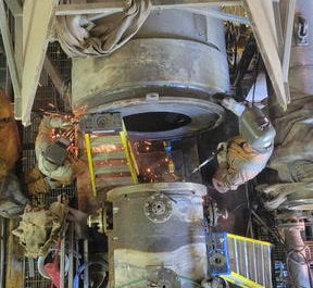 Un groupe de personnes soude un gros tuyau dans une usine.