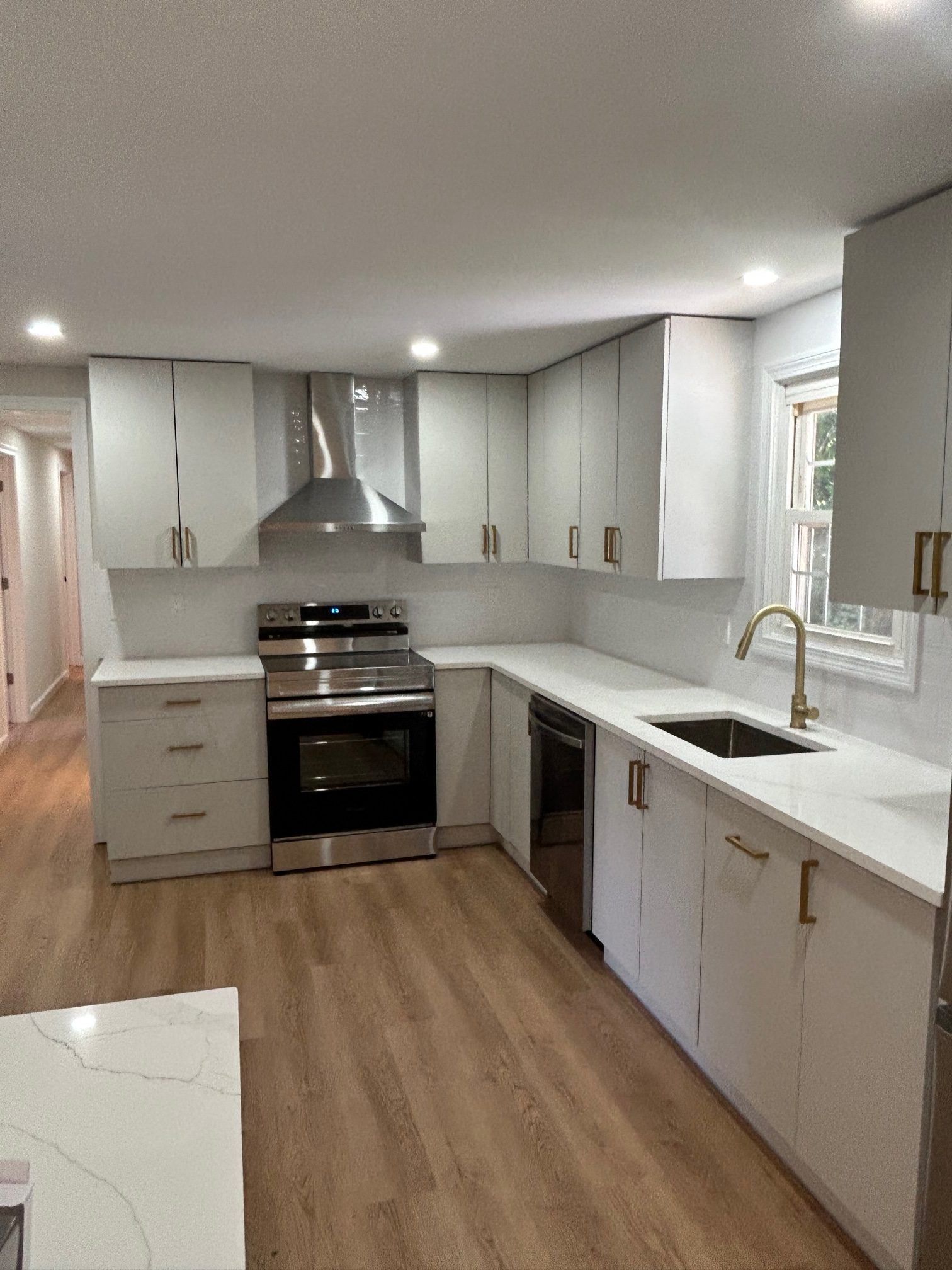 A modern kitchen with white cabinets, stainless steel appliances, light countertops, and wood-look flooring.