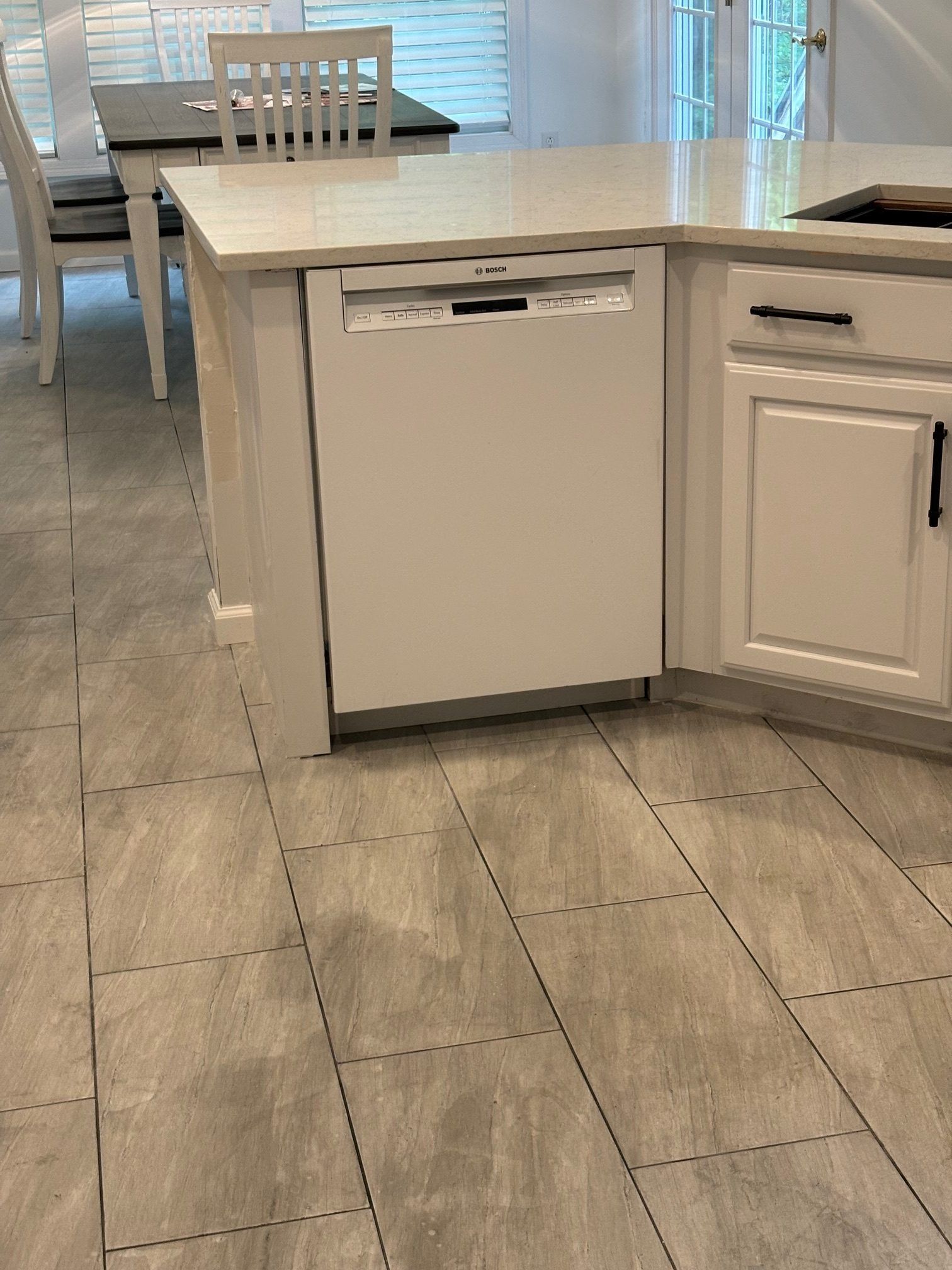 A white dishwasher integrated into a kitchen island, situated on light gray tile flooring near a dining set.