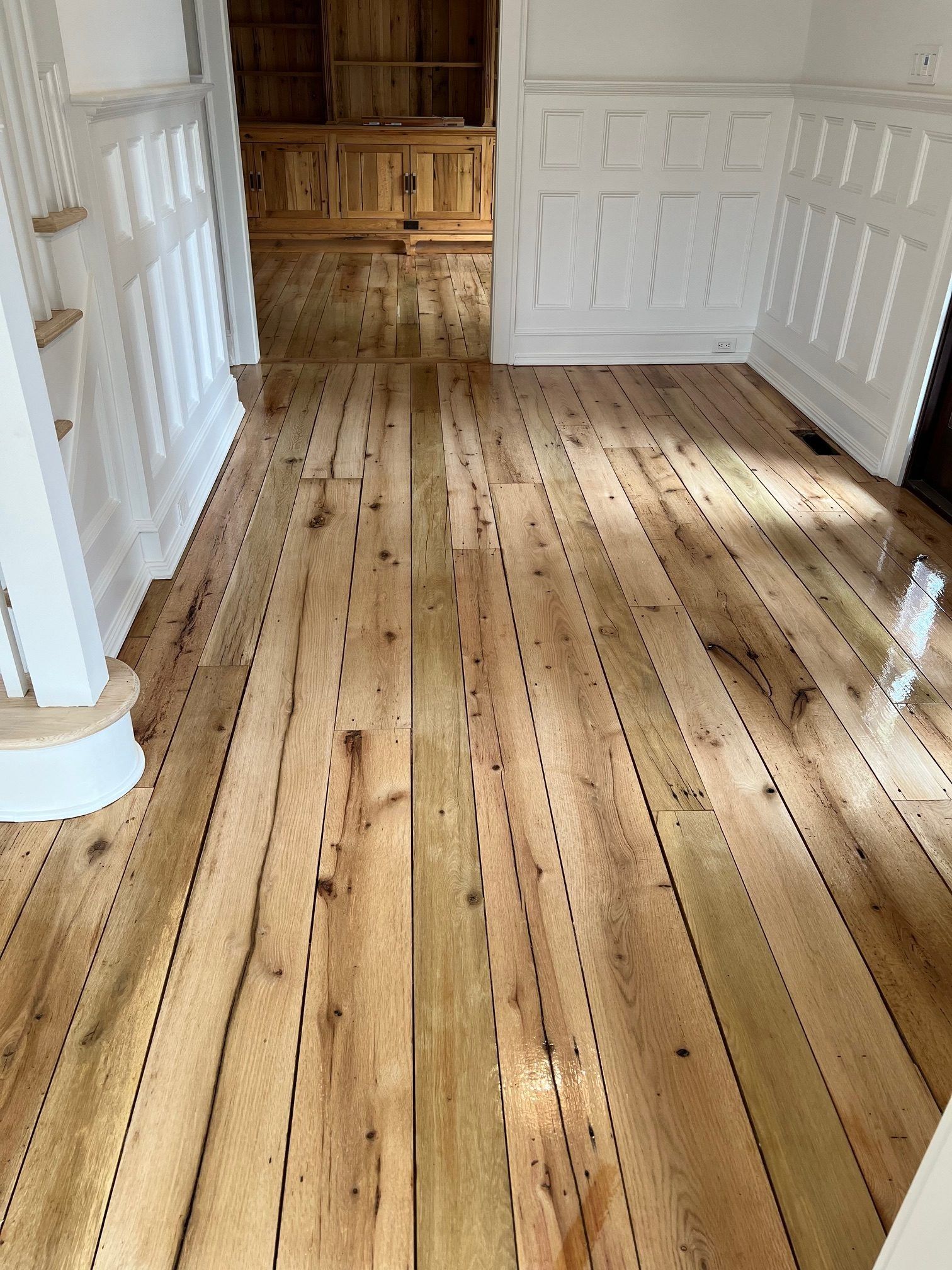 Newly installed, light-toned hardwood floors with visible nail patterns running through the seams in a house interior.