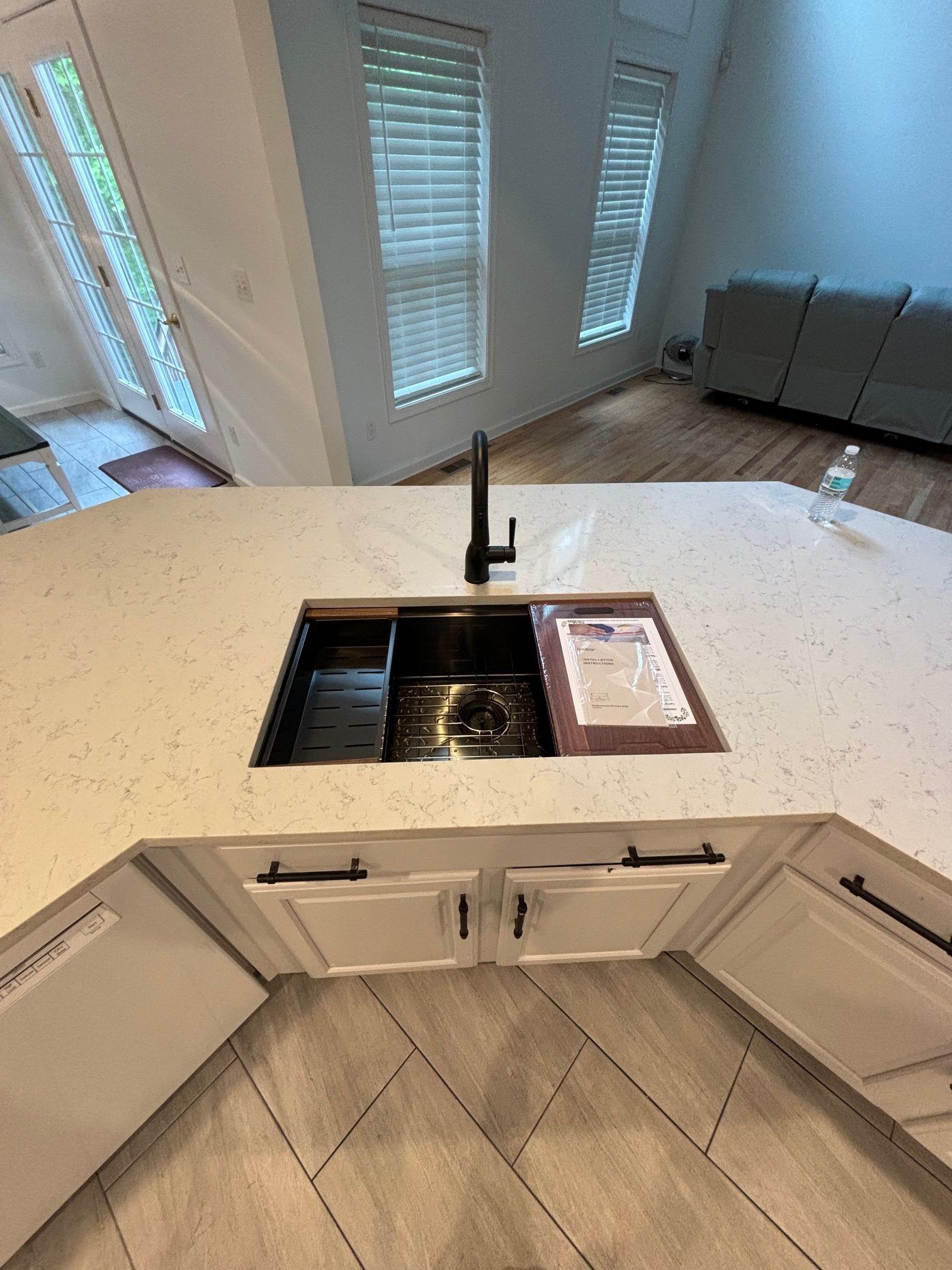 A kitchen island featuring a stainless steel workstation sink with a black faucet, set against white cabinetry and wood floors.