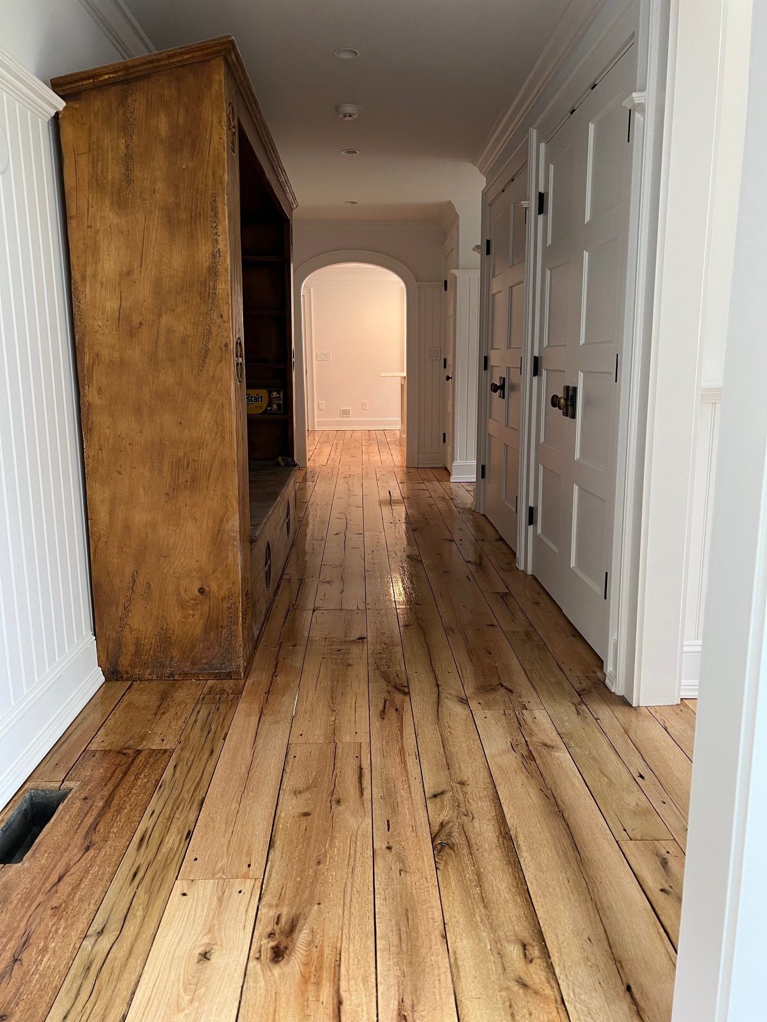 A wooden hallway with a tall antique wooden storage unit on the left and white doors leading to another room ahead.