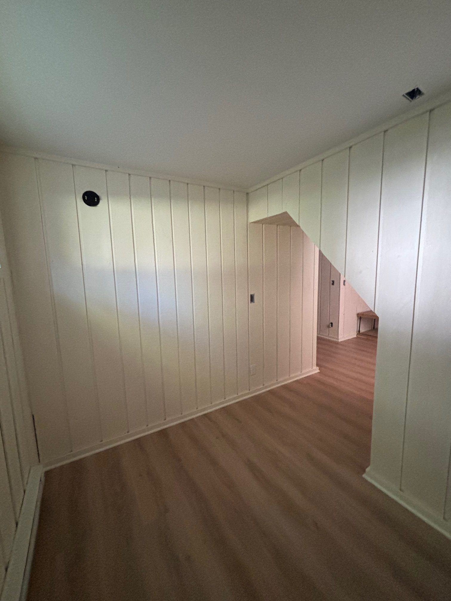 An interior view of a room with light-colored vertical paneled walls, wood-look flooring, and an arched entryway.