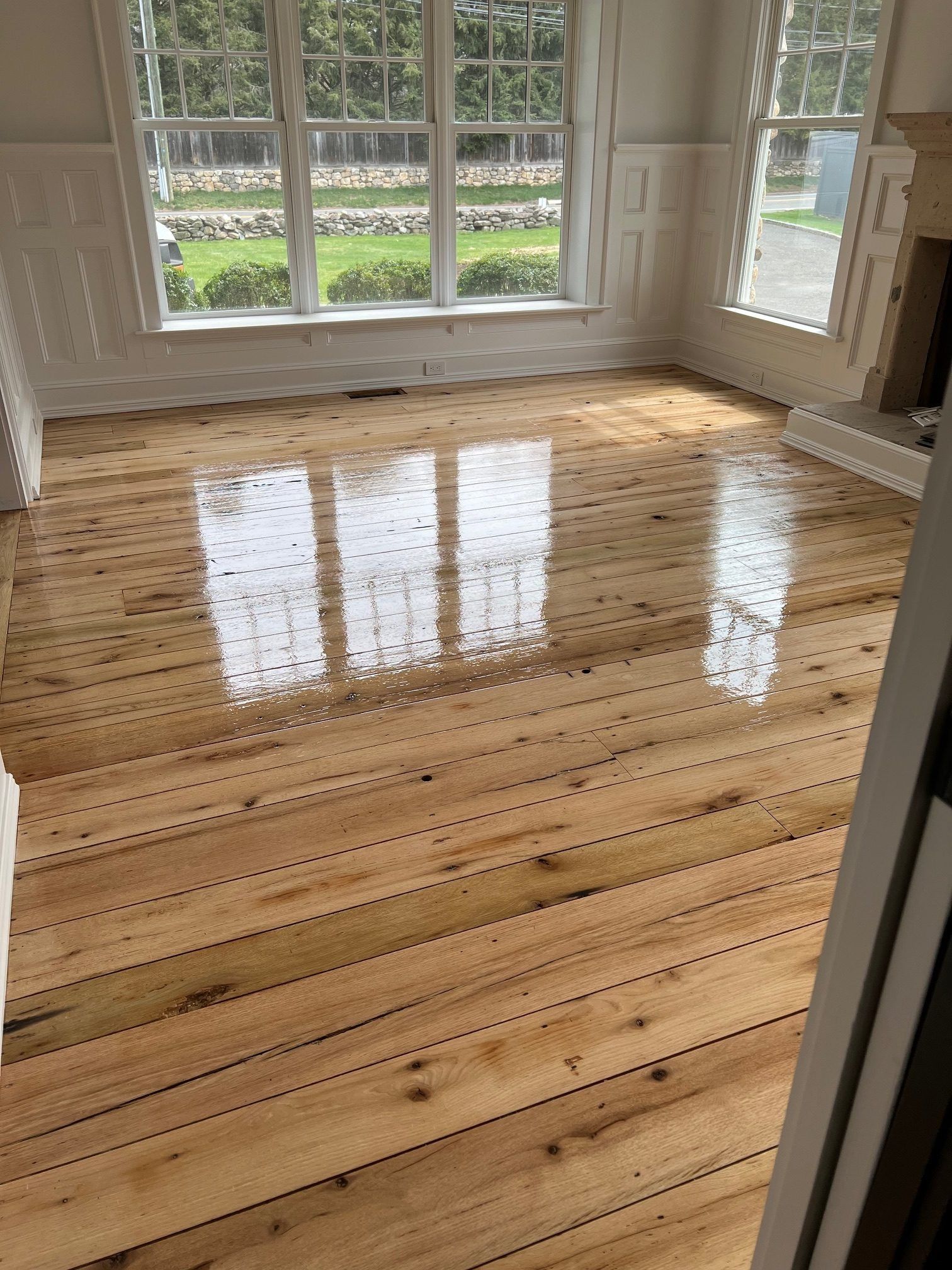 Shiny, light-colored wood floor with visible nail patterns, reflecting bright window light in an empty room.