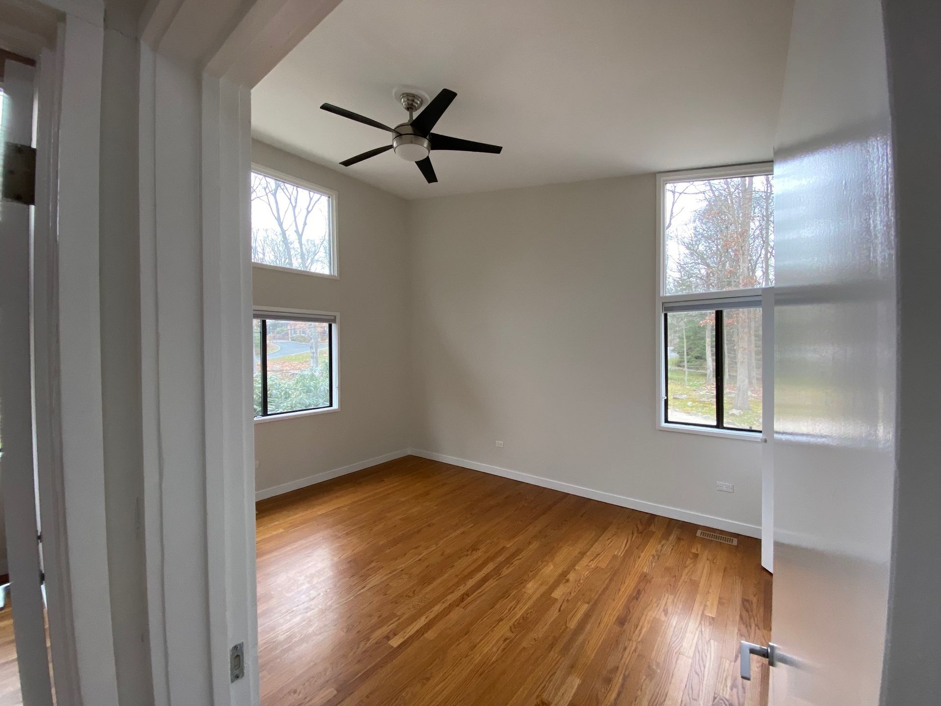 Empty room with light wood floors, high ceilings, multiple windows, and a ceiling fan.