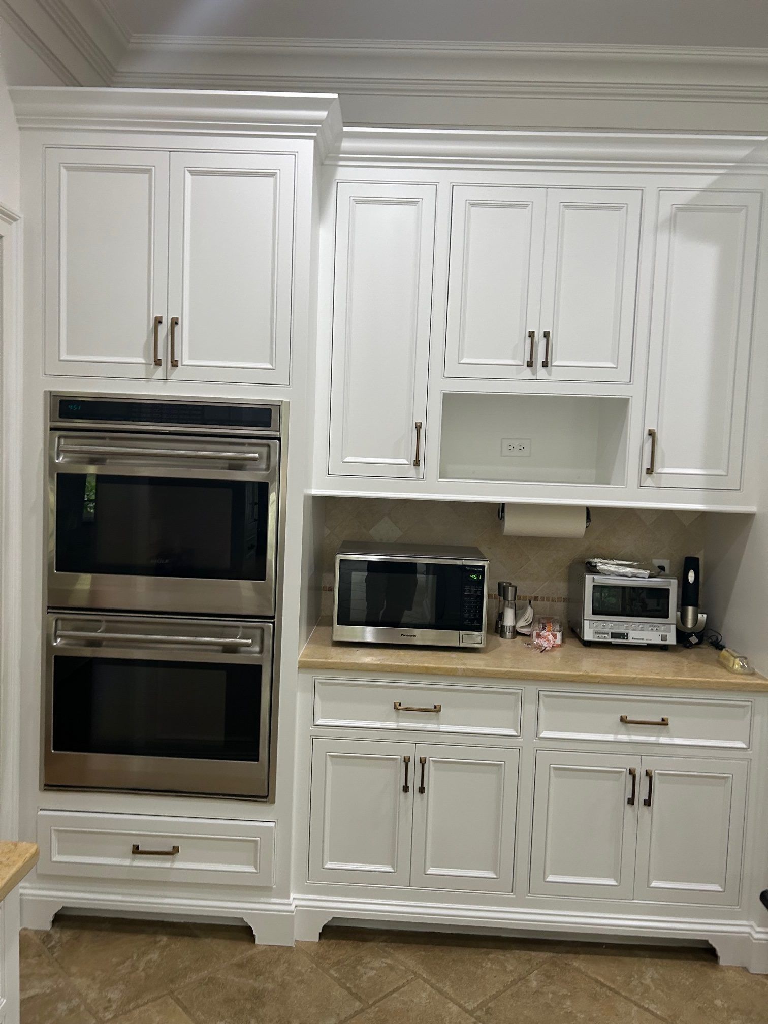 White kitchen cabinetry featuring a double oven, countertop microwave, toaster, and under-cabinet storage.