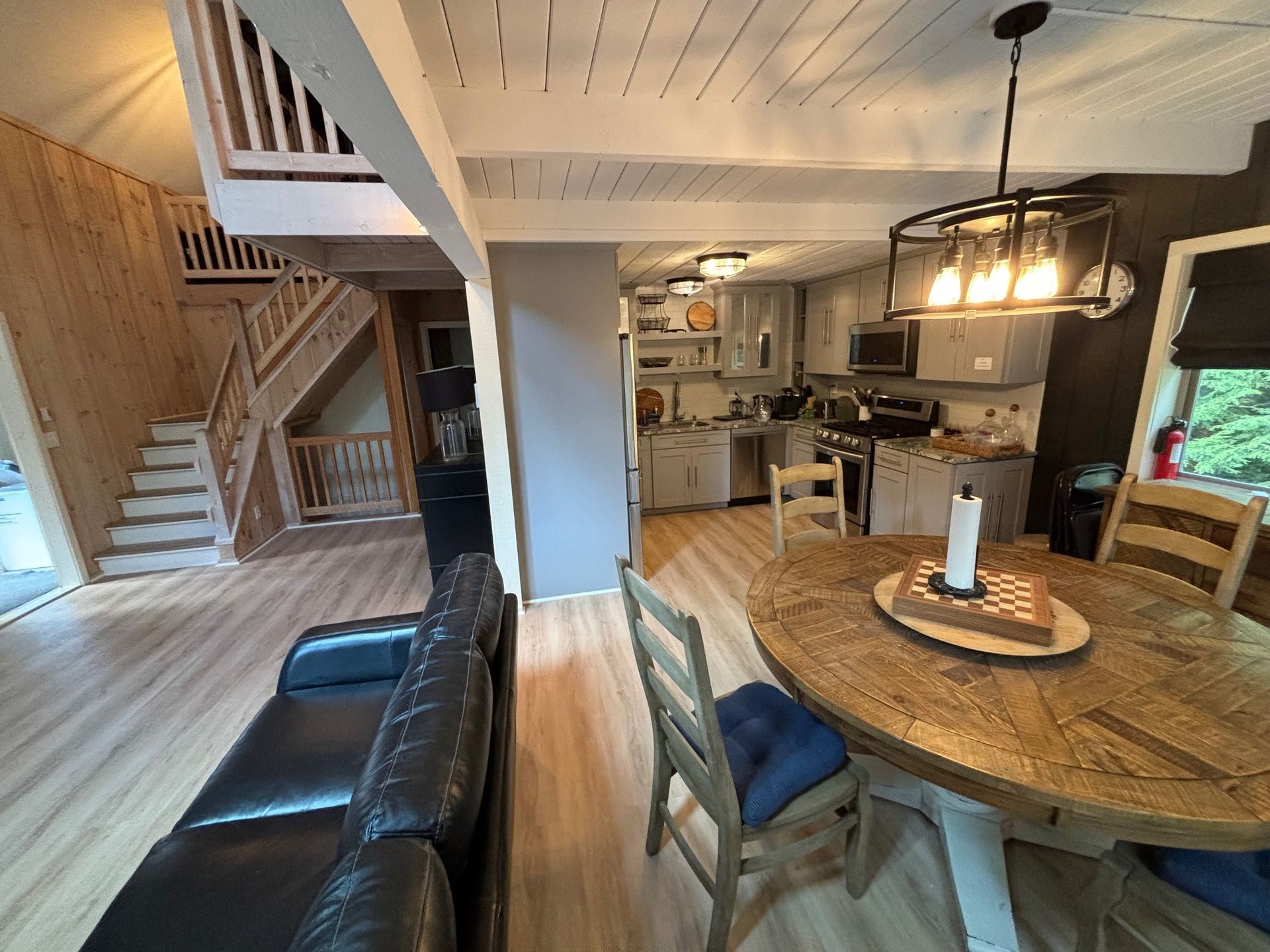 A wood-paneled home interior featuring a circular dining table, a black leather sofa, and a staircase leading upstairs.