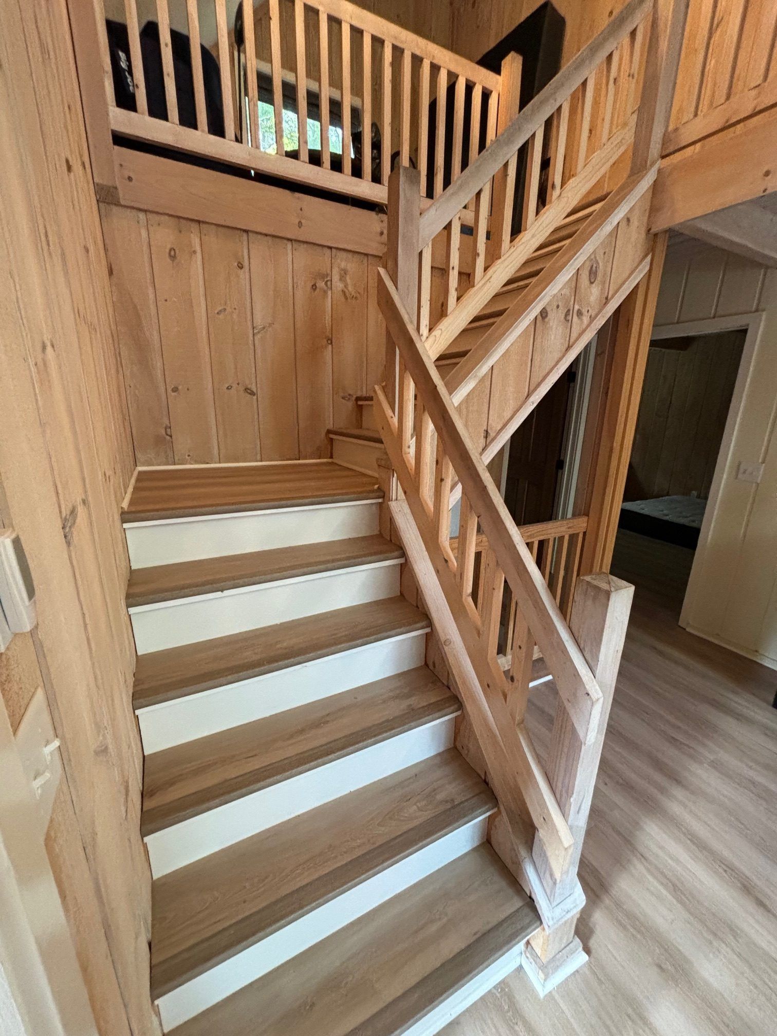 A wooden staircase with white risers and a matching railing leading to an upper landing in a light-toned interior.