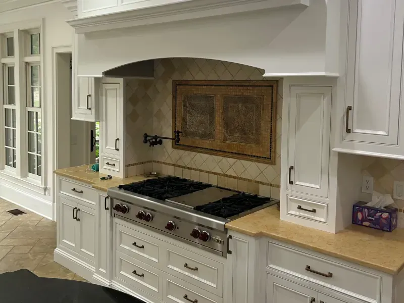 White kitchen featuring a gas range stove with a range hood and a decorative tiled backsplash.