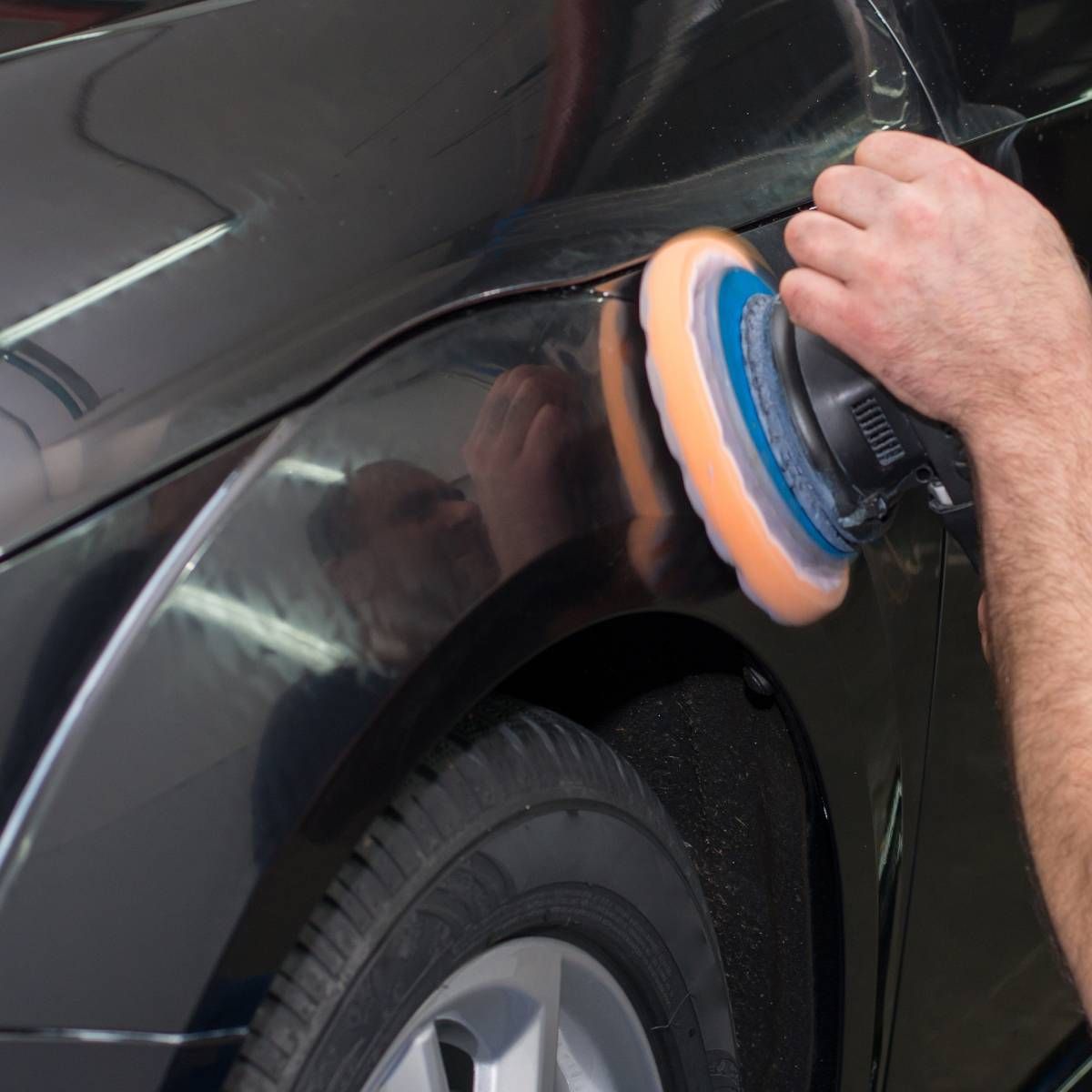 Person polishing a black car with an electric polisher.