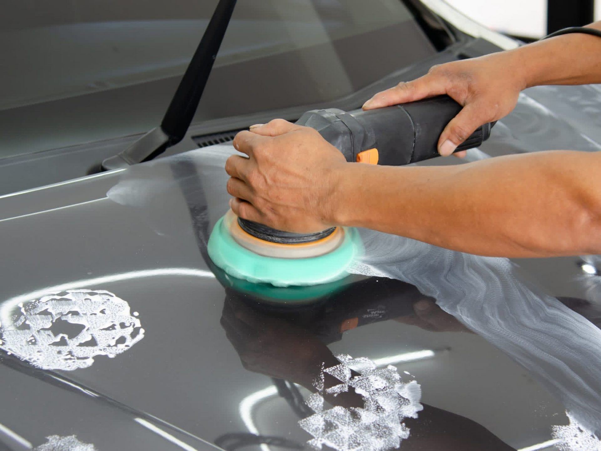 A person is polishing the hood of a car with a machine.