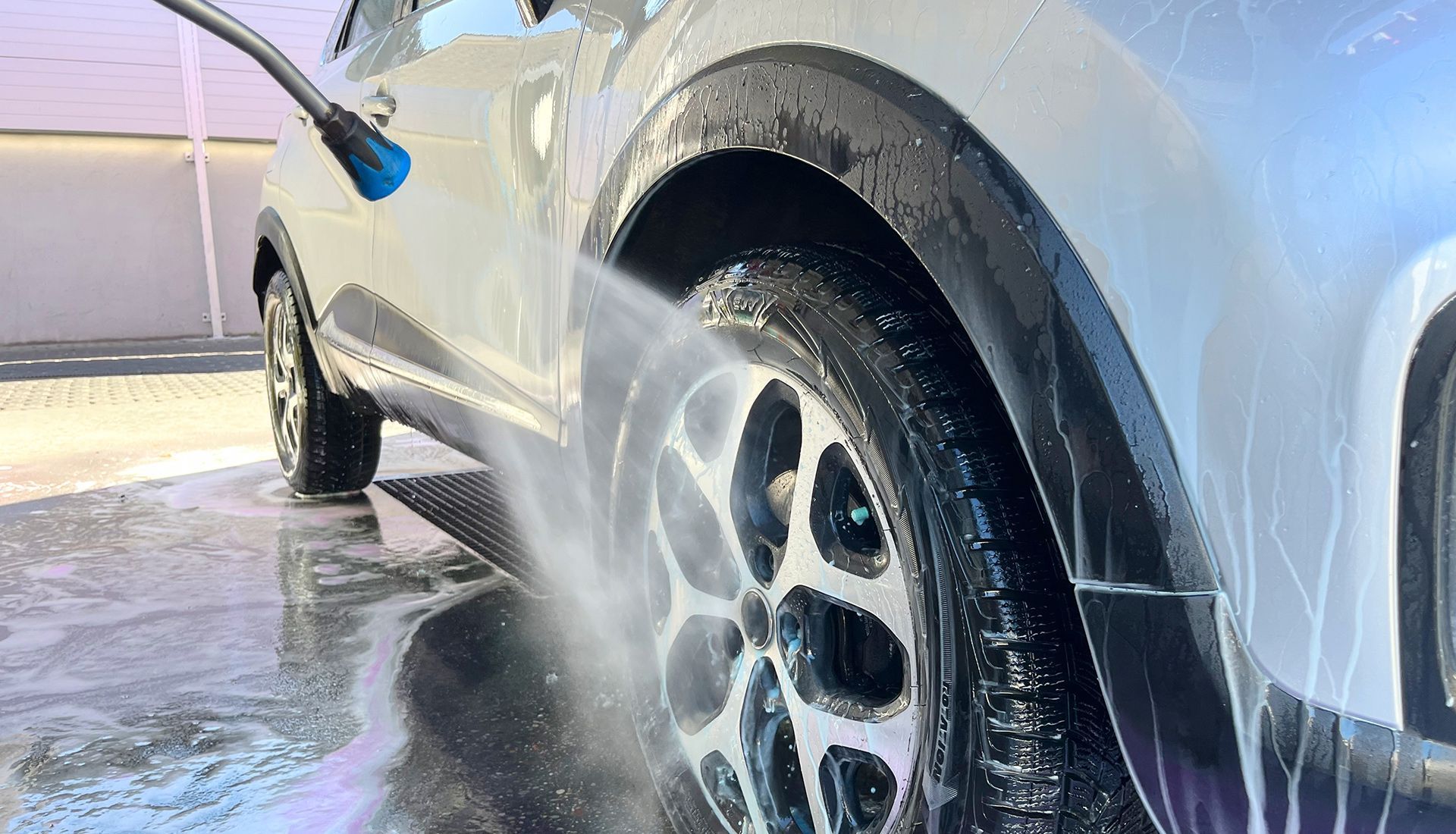 A car is being washed with a high pressure washer at a car wash.