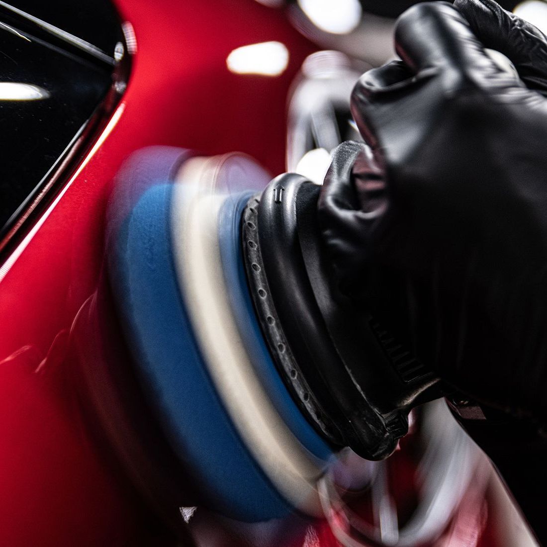 A person is polishing a red car with a polisher.
