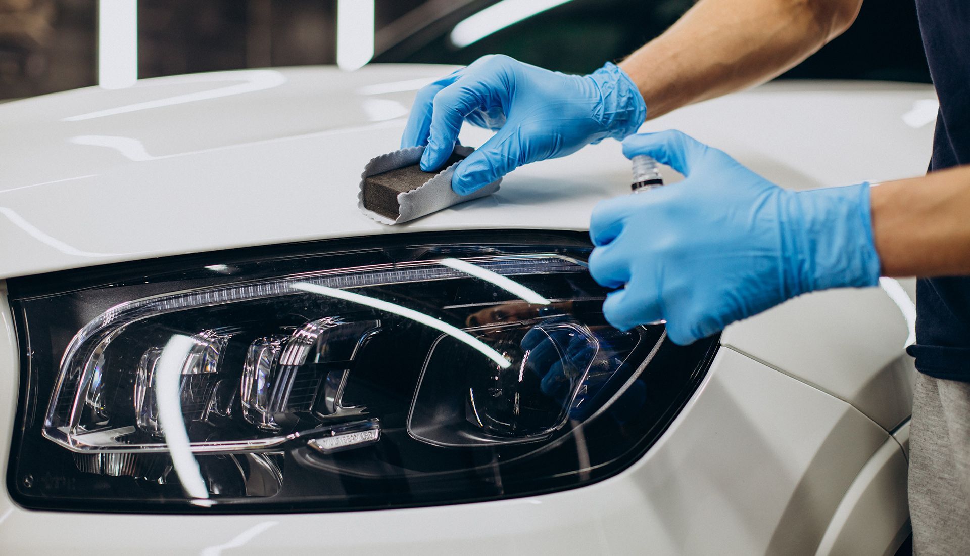 A person wearing blue gloves is polishing the headlight of a white car.