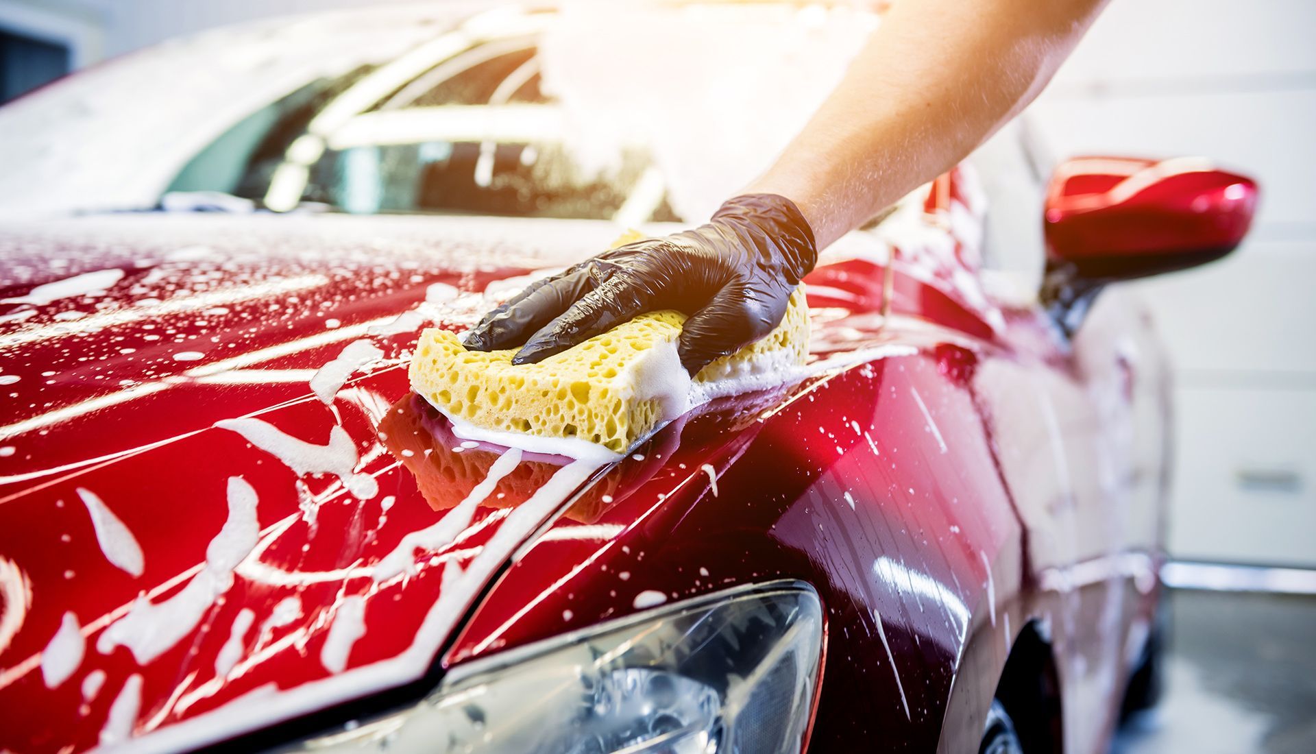 A person is washing a red car with a sponge.