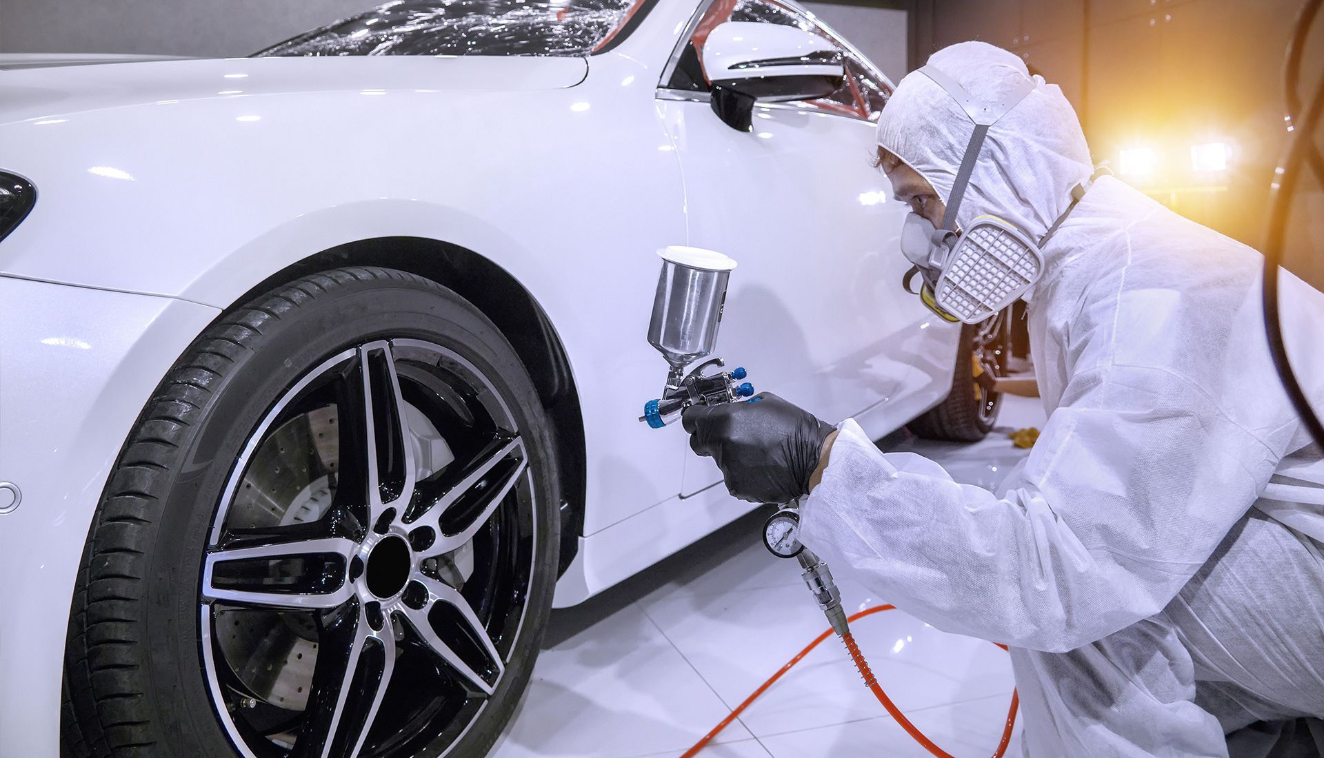 A man in a protective suit is spray painting a white car.